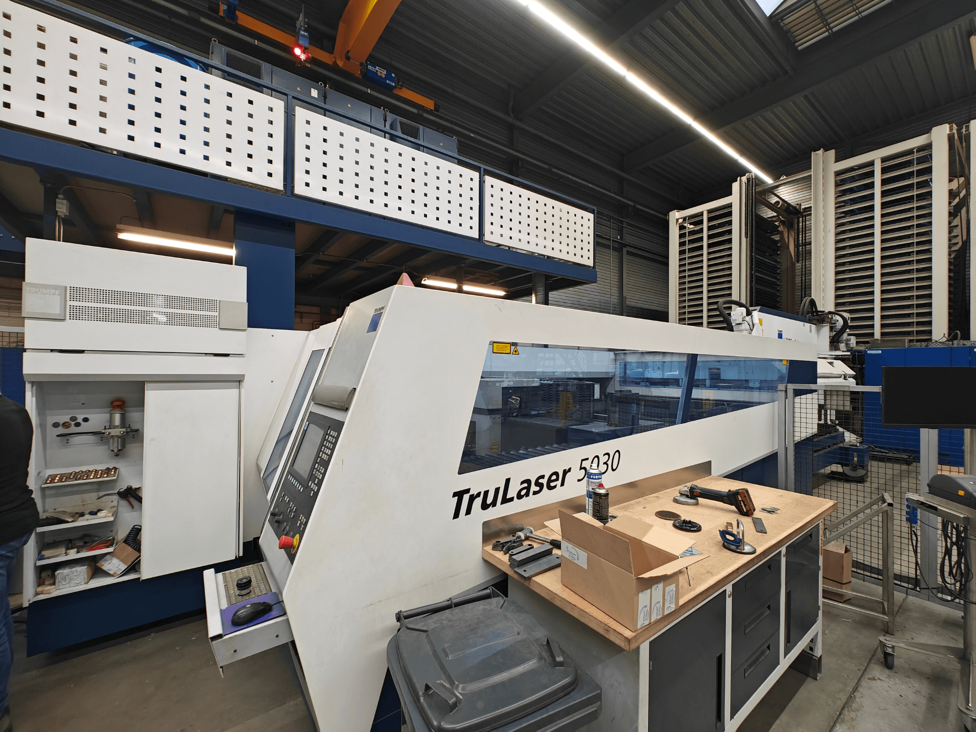 TruLaser 5030 Maschine in einer Werkstatt, Frontansicht mit sichtbarem Bedienfeld, umgeben von Werkzeugen und Geräten.