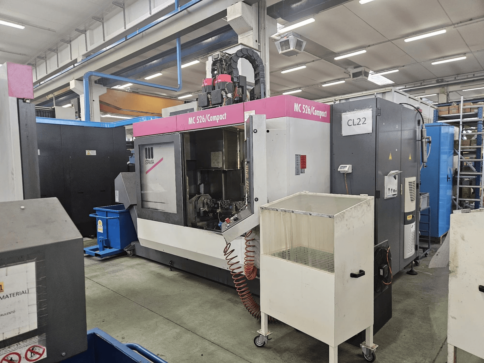 MC 526 Compact CNC-Maschine von Stama, Seitenansicht, zeigt Bedienfeld, Kühlmitteltank und angrenzende Maschinen.