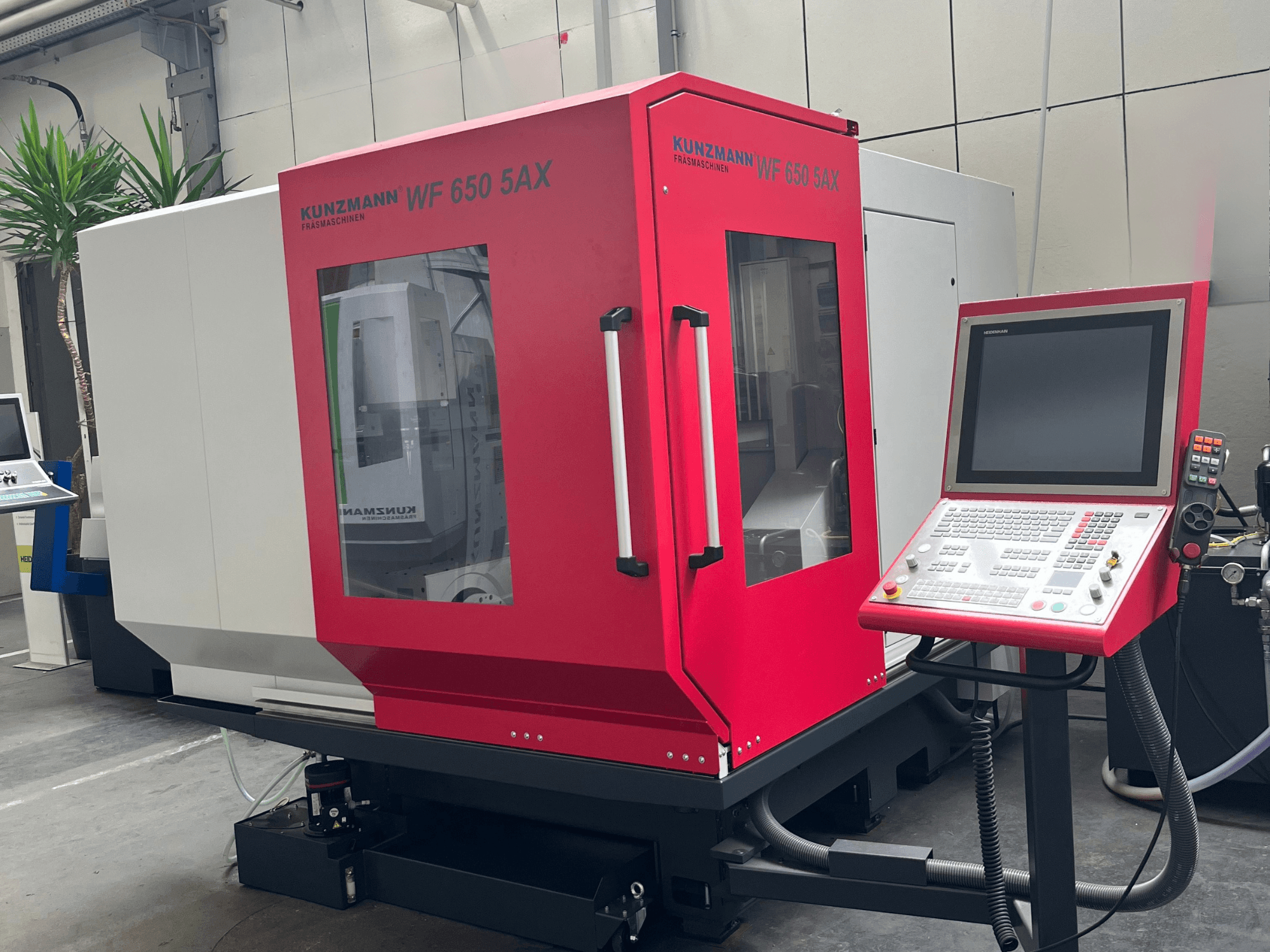 Vertikales Bearbeitungszentrum KUNZMANN WF 650 5AX in Rot, Vorderansicht mit Bedienfeld und Touchscreen, in einer Werkstatt aufgestellt.
