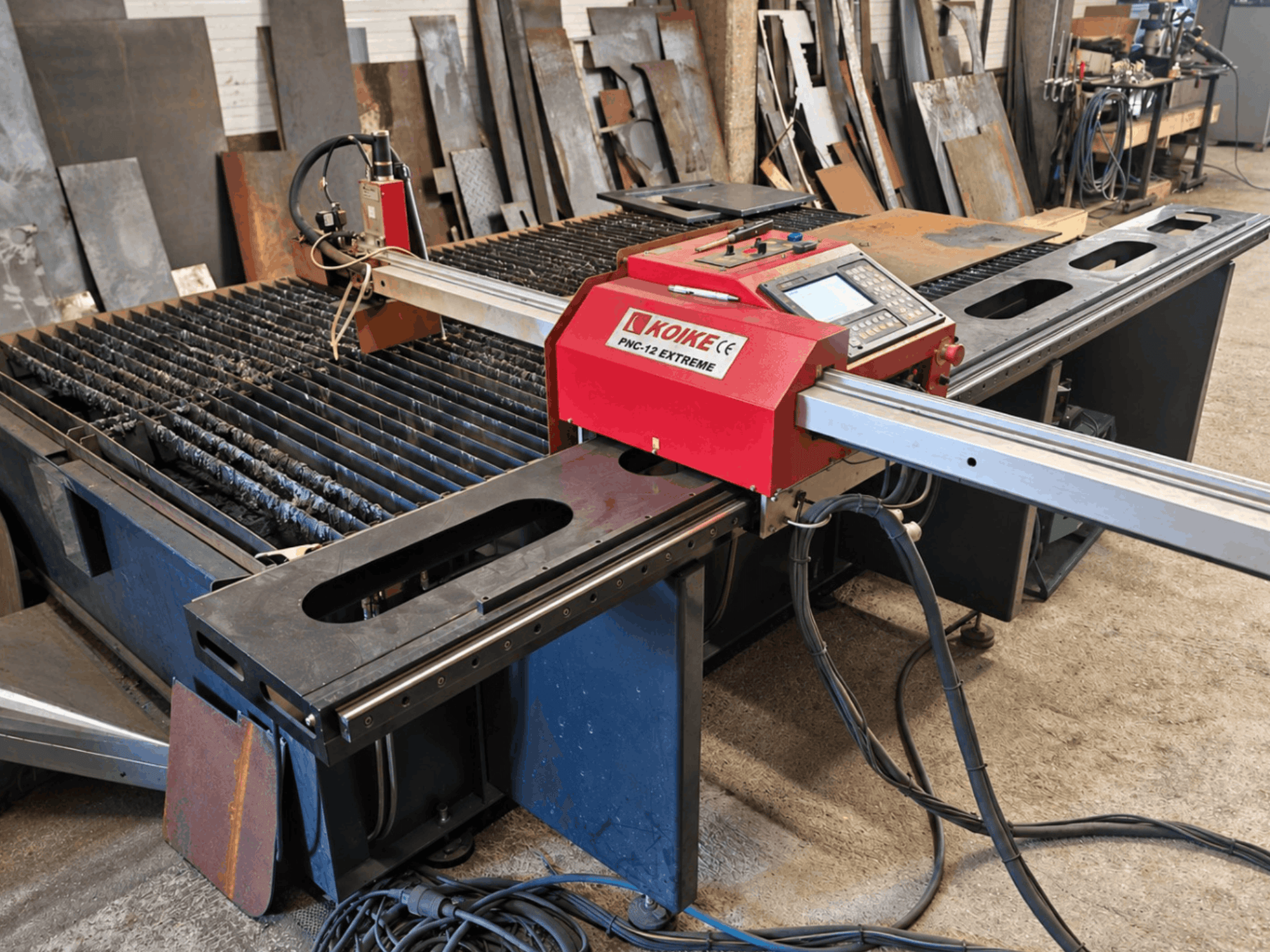 Vorderansicht der Plasmaschneidemaschine KOIKE PNC-12 Extreme mit Metallschneidetisch, Bedienfeld und Kabeln.