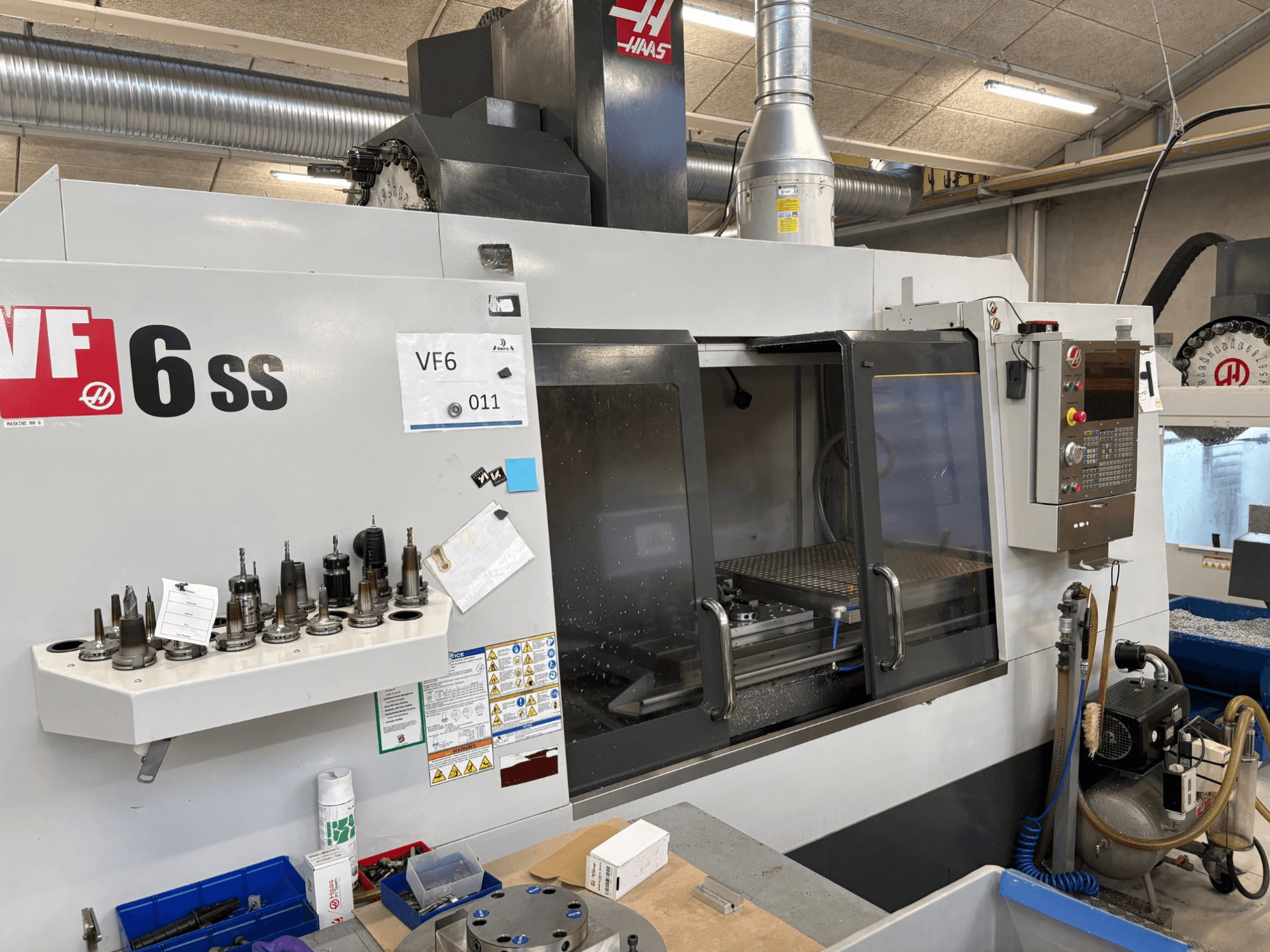 Haas VF-6 SS CNC-Fräsmaschine, Vorderansicht. Mit verschiedenen Werkzeugen, Bedienfeld und sichtbarem internen Arbeitsbereich.