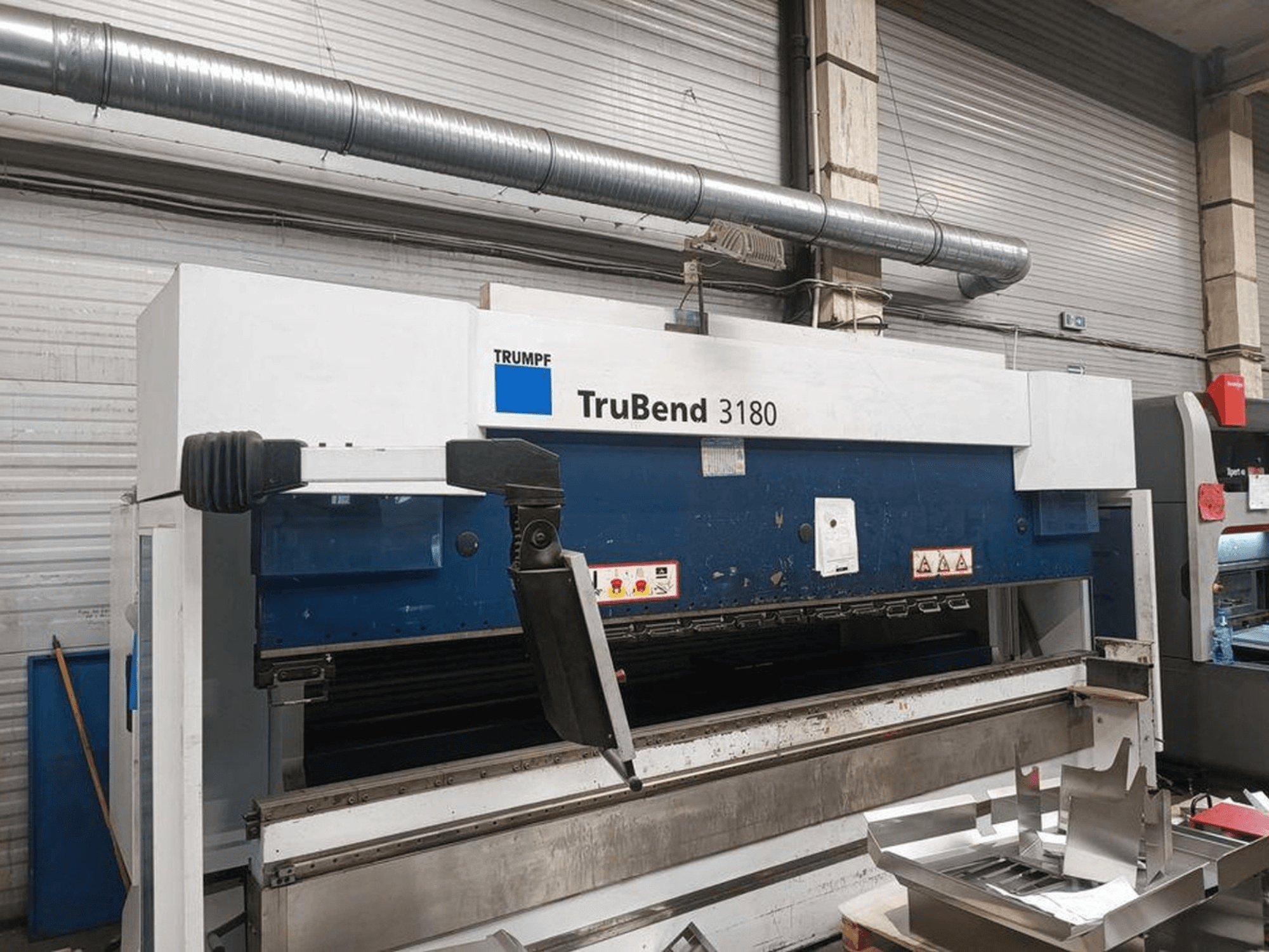 Trumpf TruBend 3180 Biegemaschine in einer Werkstatt, Seitenansicht mit Bedienfeld und Metallteilen auf dem Tisch.