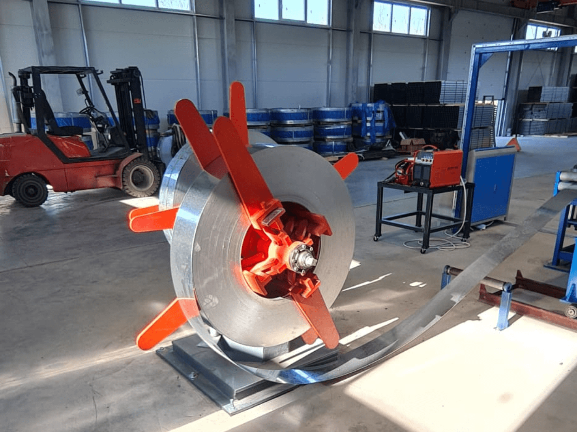 Metallspule mit roten Griffen auf einem Ständer, aus einem Winkel betrachtet. Industrieller Hintergrund mit Maschinen und einem Gabelstapler.