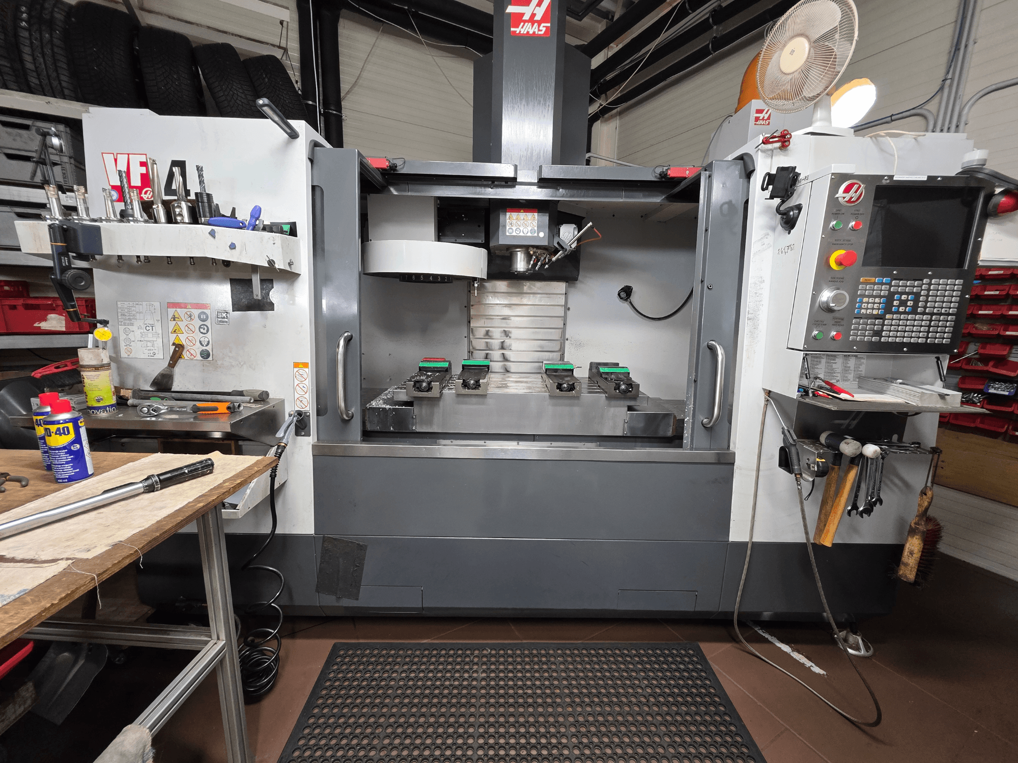 Frontansicht der Haas VF-4 CNC-Fräse in einer Werkstatt, mit Werkzeugen, einer Computerschnittstelle und zwei Werkstücken auf dem Tisch.