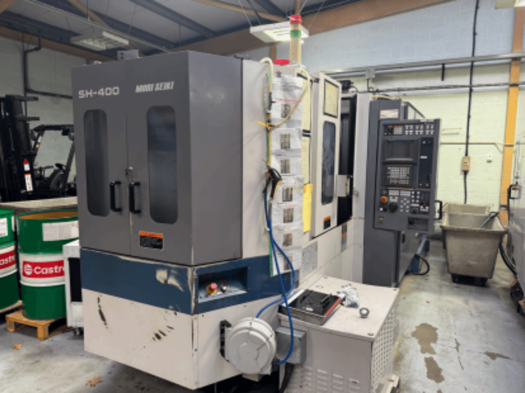 Moni Seiki SH-400 CNC-Maschine, Seitenansicht mit Bedienfeld, Türen und Industrieumgebung.