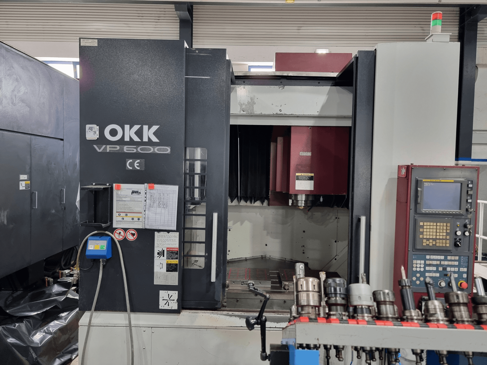 Das vertikale Bearbeitungszentrum OKK VP600 in der Vorderansicht, mit Blick auf das Bedienfeld und die Werkzeughalter auf einem Gestell.