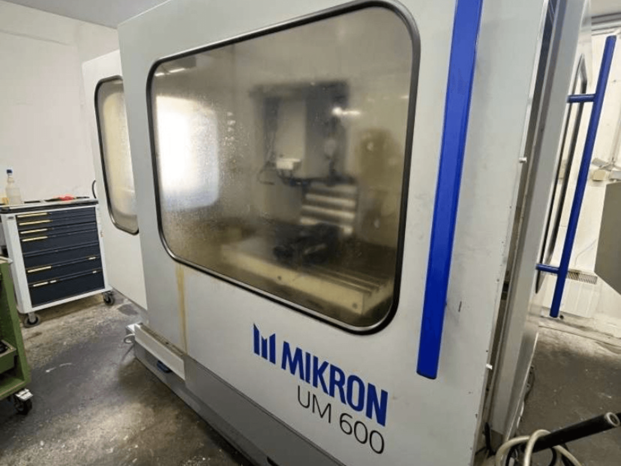 MIKRON UM 600 TNC 410/426 Universal-Bearbeitungszentrum, Seitenansicht, mit beschlagenem Glas und sichtbarer Werkzeugablage in der Nähe.