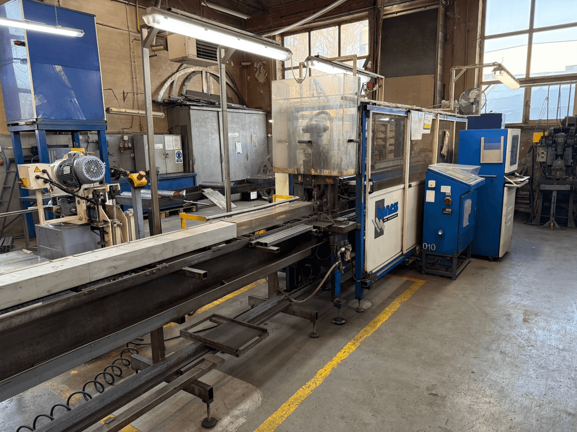 Industrielle Werkstatt mit einer blauen Haweas-Maschine, Seitenansicht mit Förderband und Ausrüstung in einem großen, gut beleuchteten Raum.