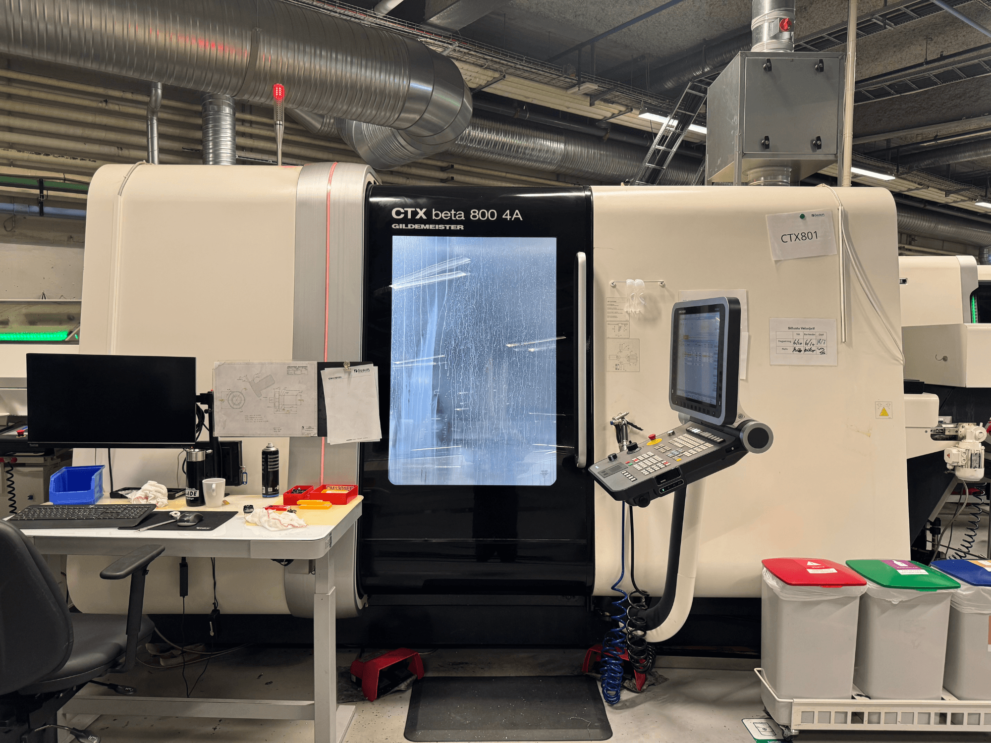 CTX beta 800 4A Maschine mit Bedienfeld und Monitor, Seitenansicht, in einer Werkstatt mit Büroeinrichtung und farbigen Mülleimern.