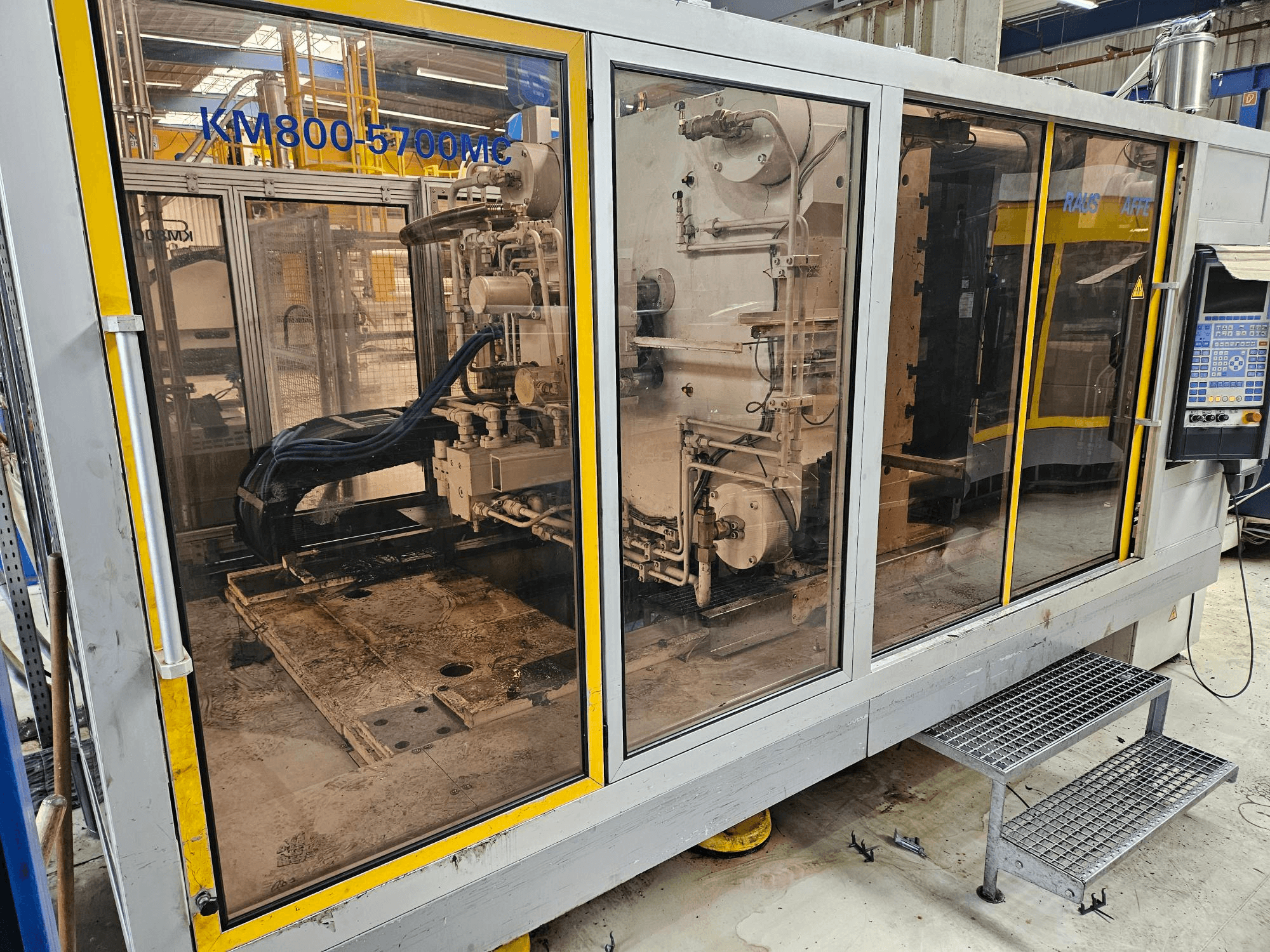 Hydraulische Spritzgießmaschine Krauss Maffei KM800-5700 MC, Vorderansicht mit durch Glaswände sichtbaren Bauteilen.