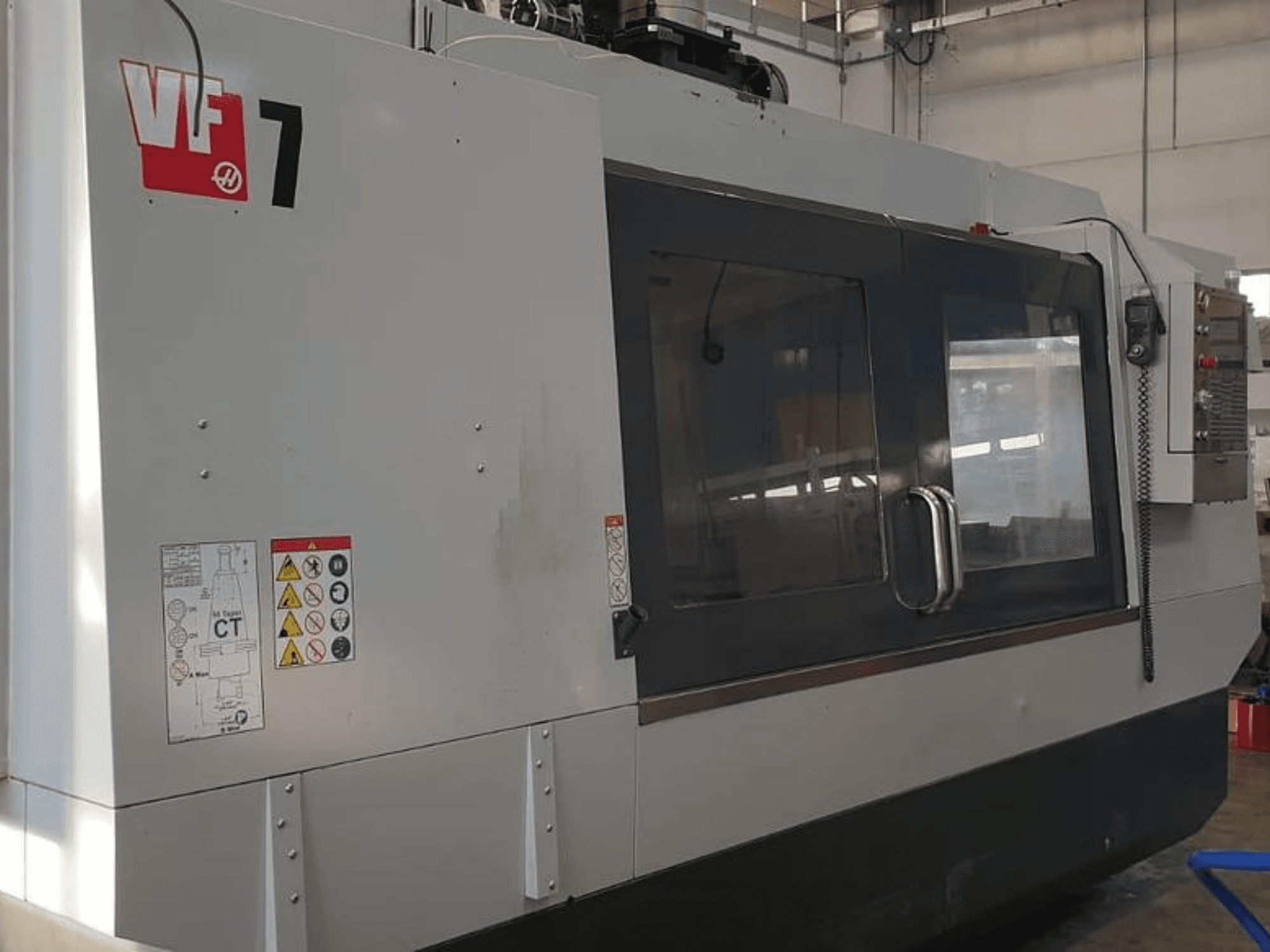 Haas VF-7 CNC-Maschine in der Seitenansicht, mit metallgrauer Oberfläche, Bedienfeld und Sicherheitsschildern.