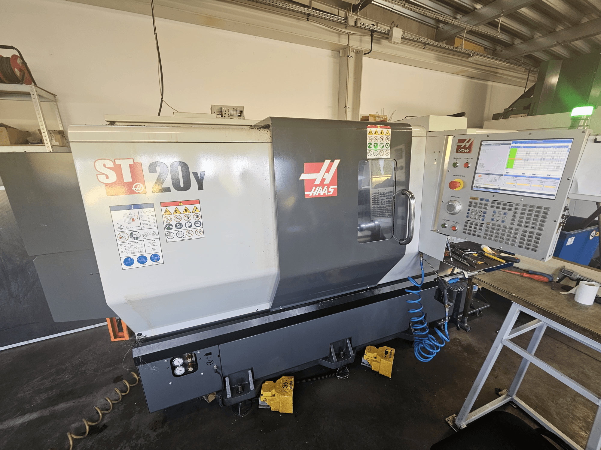Haas ST-20Y CNC-Drehmaschine in der Vorderansicht mit Bedienfeld; mit Sicherheitsaufklebern und Luftschlauchdetails an der Seite.