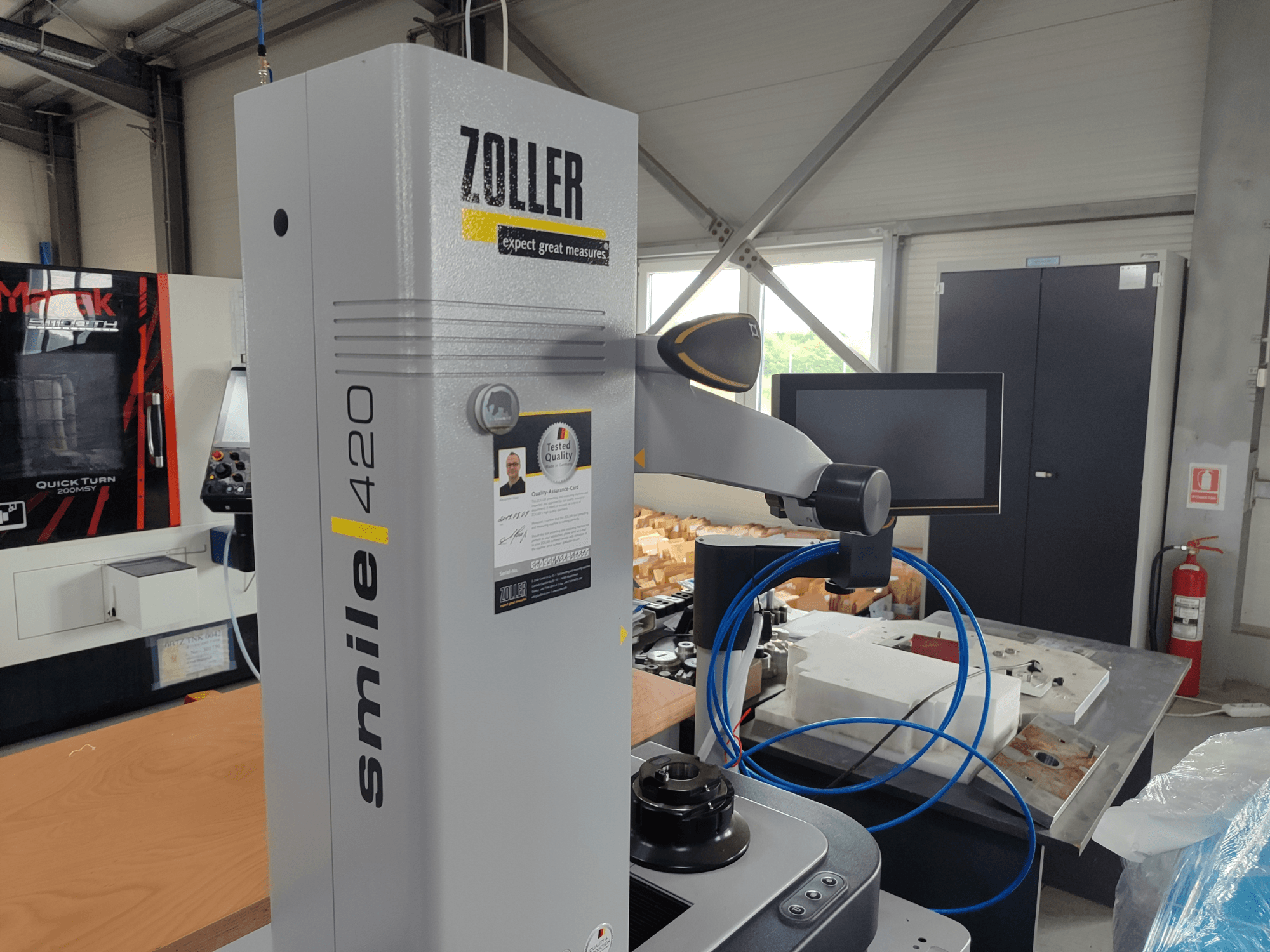ZOLLER smile 420 Messgerät mit Monitor, Seitenansicht in einer Werkstatt, mit blauen Schläuchen und Maschinen im Hintergrund.