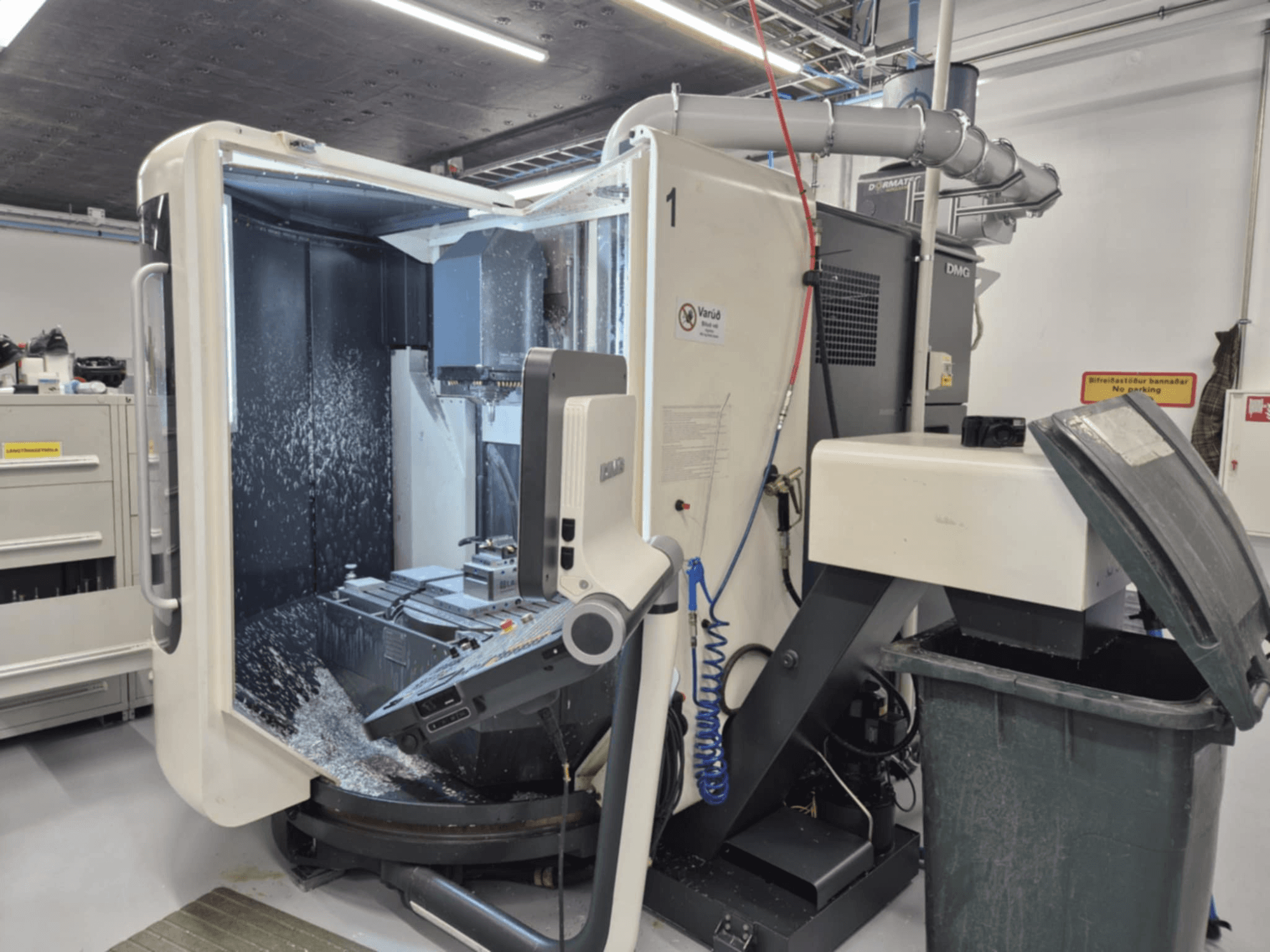 Geöffnete DMG-Fräsmaschine mit Kühlmittelnebel, mit Metallspänen und Werkzeugkontrollen, von vorne gesehen.