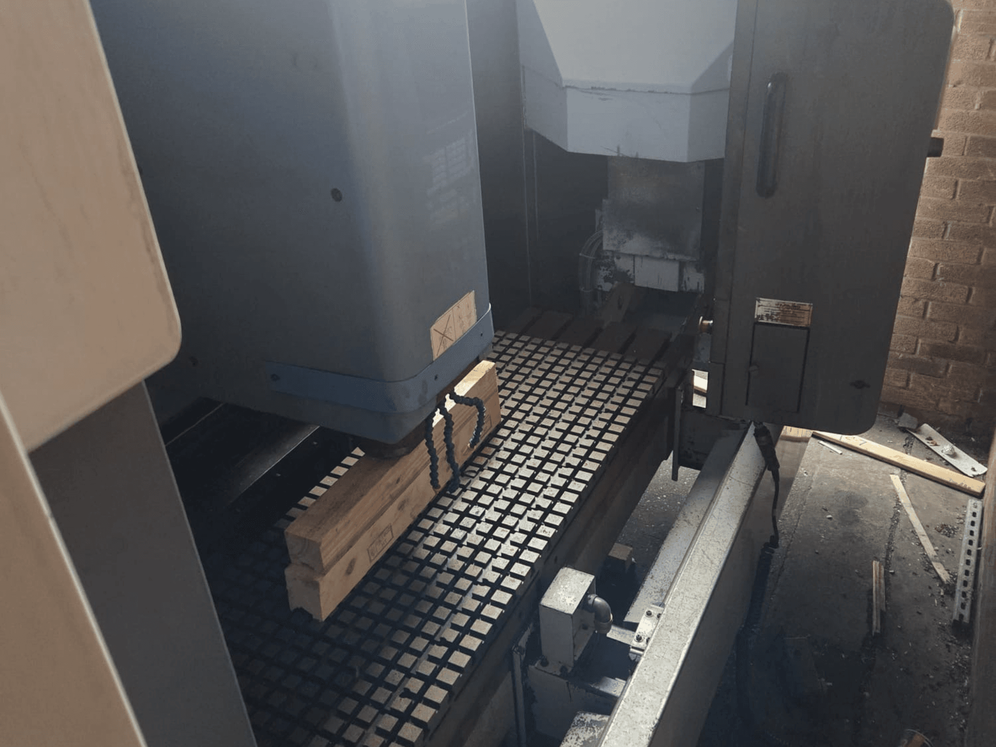 Frontansicht einer CNC-Maschine mit Holzbrettern auf einem Rastertisch, mit Werkzeugen und Bedienelementen an der Seite.