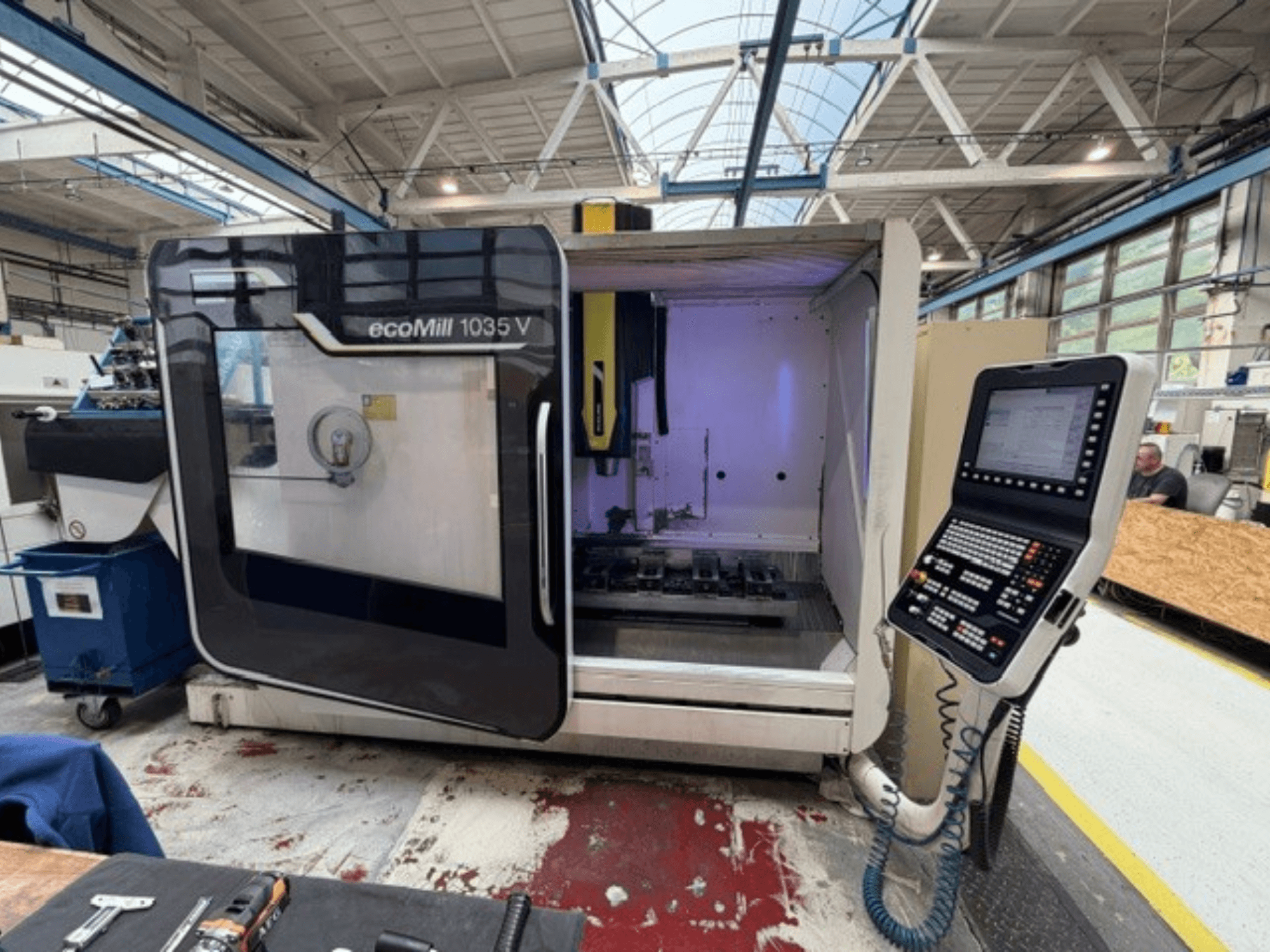 Vorderansicht des vertikalen Bearbeitungszentrums DMG MORI ecoMill 1035V bei geöffneter Tür, die den Bedienpultbereich und den Arbeitsbereich im Inneren zeigt.