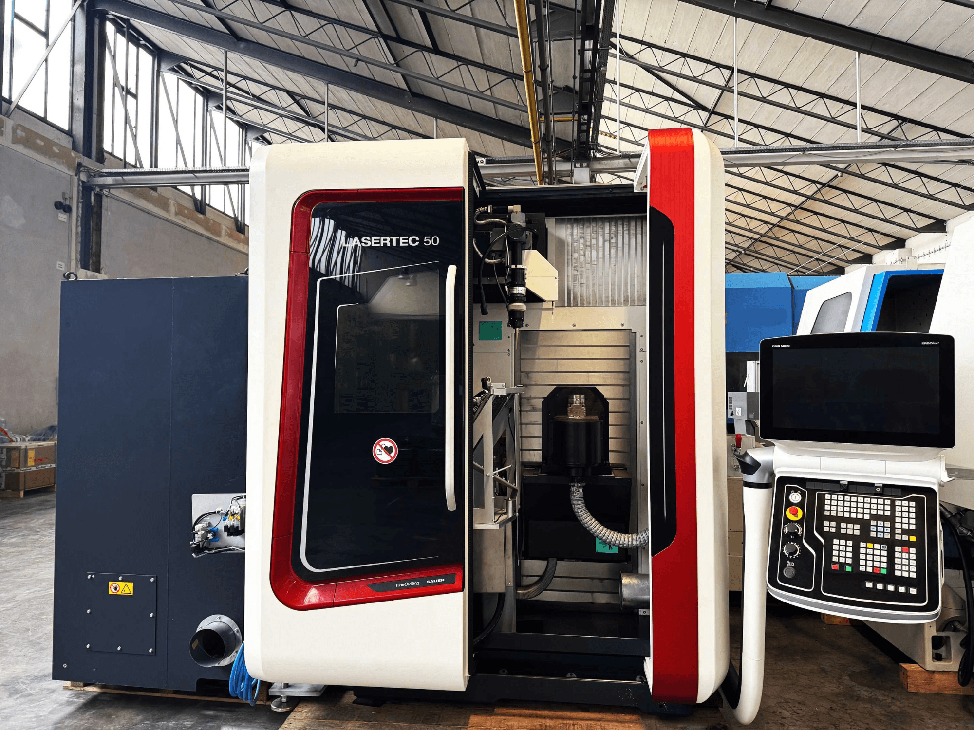 LaserTec 50 CNC-Maschine in der Seitenansicht, mit schwarz-weißem Bedienfeld, sichtbarem Werkzeughalter und Industrieumgebung.