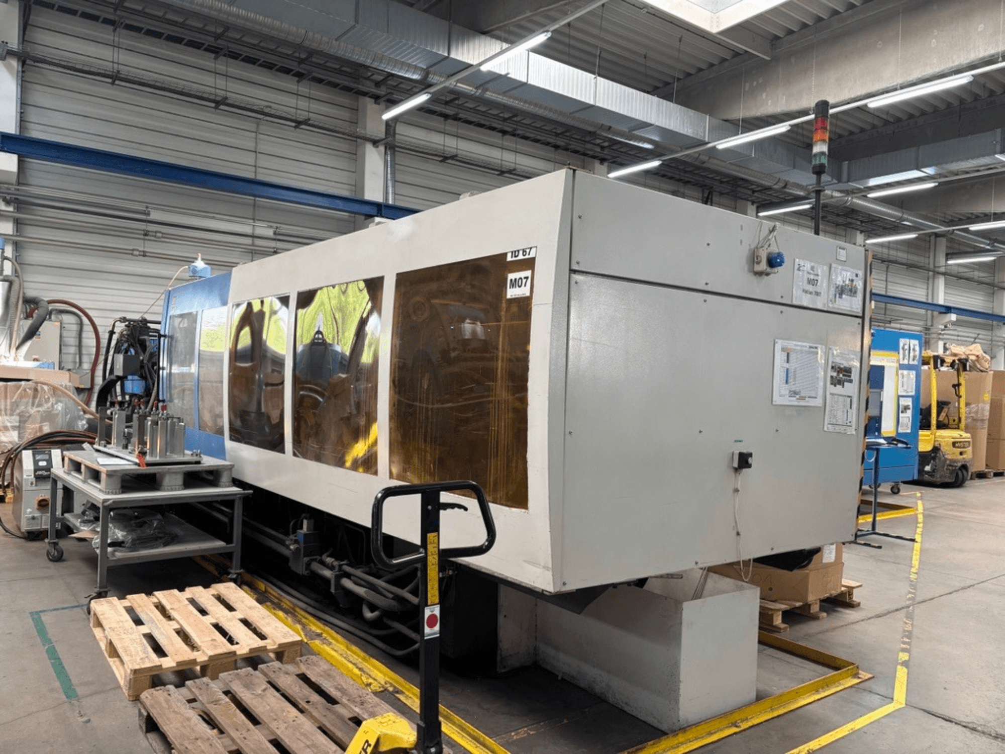 Hydraulische Spritzgießmaschine vom Typ HAITIAN 7000/5000 in einer Fabrik, Seitenansicht mit sichtbaren Bedienfeldern und Sicherheitsleuchten.