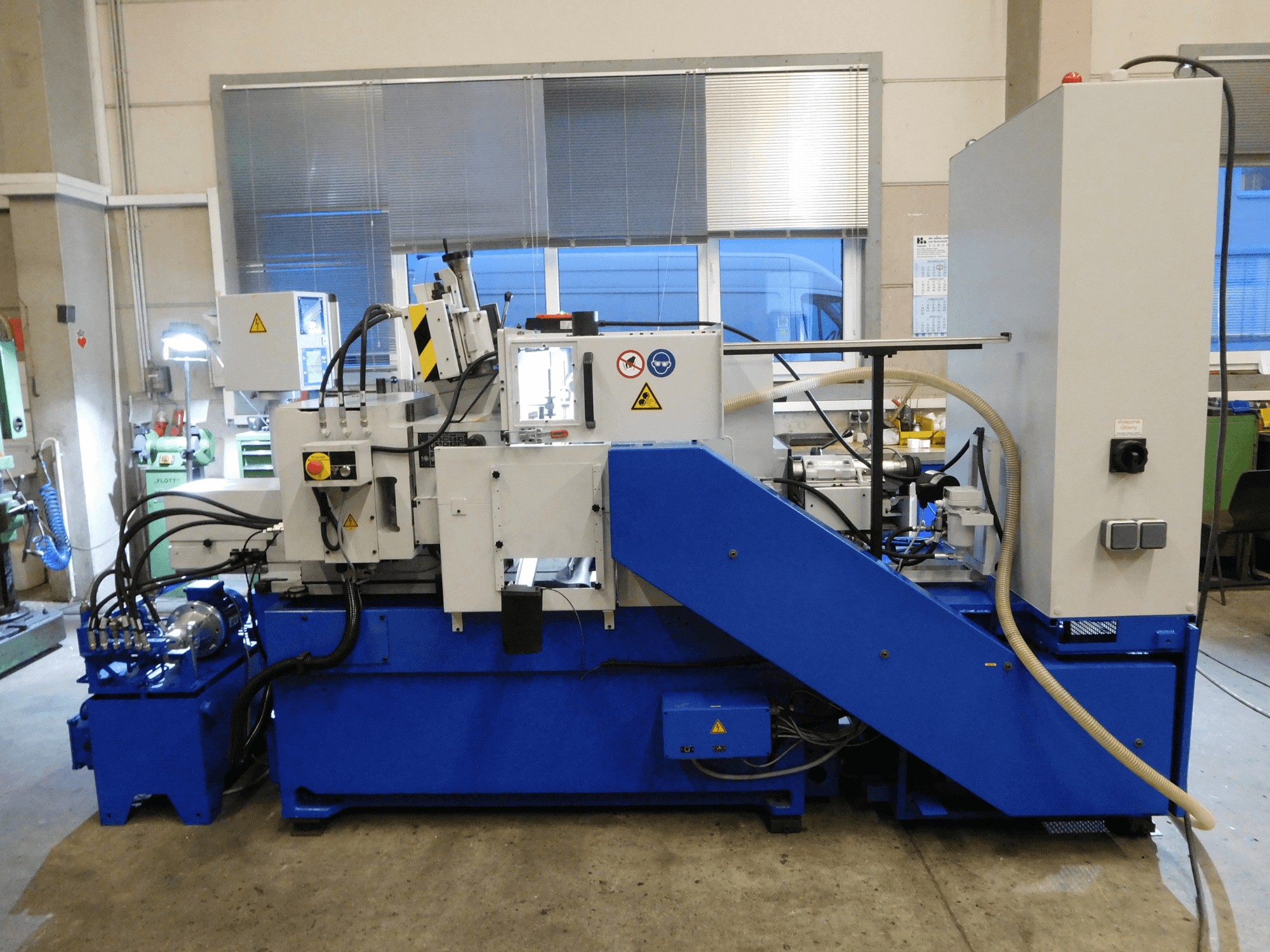 Schaudt Mikrosa SASL 125 spitzenlose Schleifmaschine, Seitenansicht, mit blauem Sockel und Bedienpult, mit Darstellung der Betriebsfunktionen.