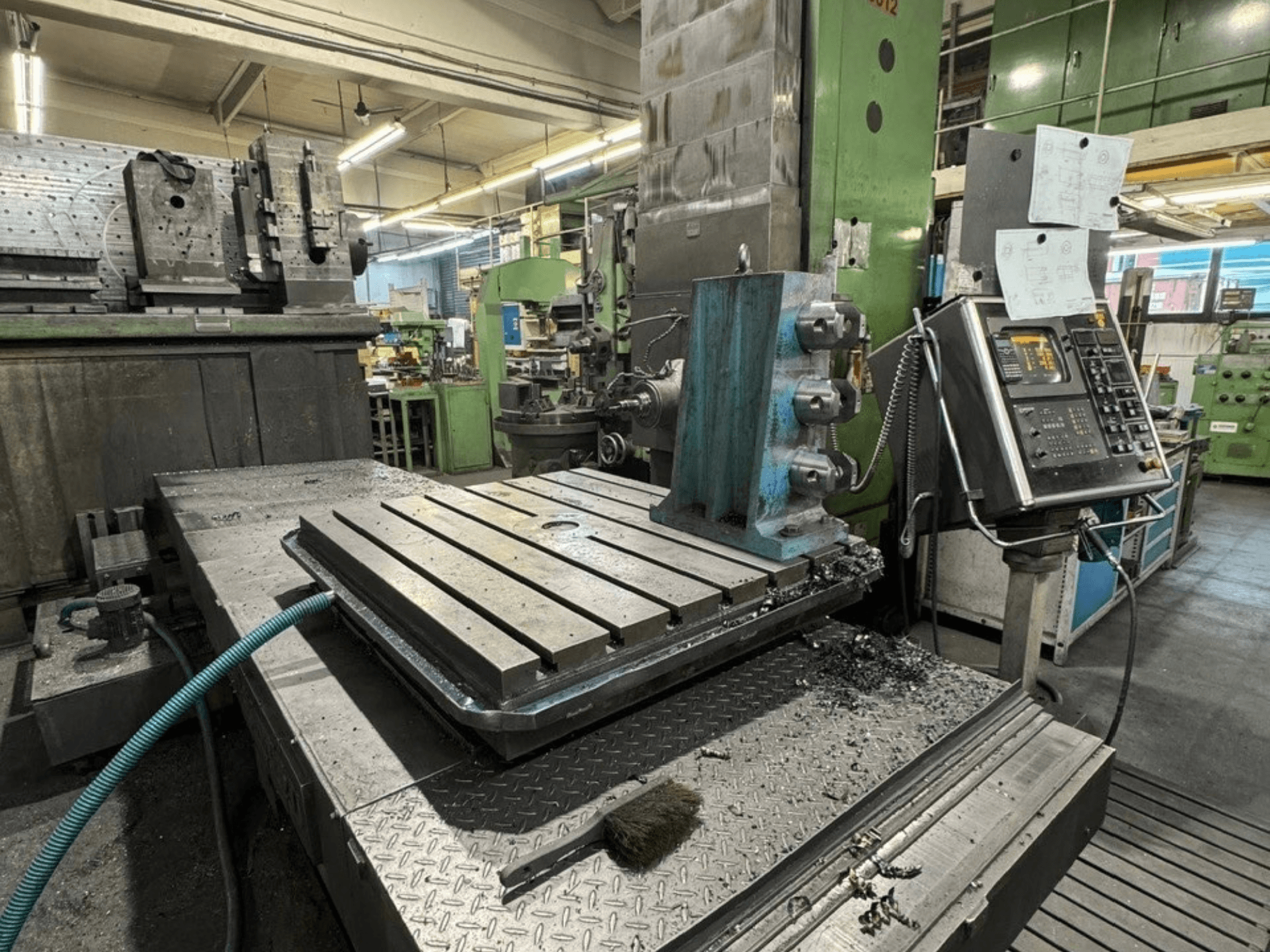 JUARISTI 12/TS1.7 Bohrmaschine in einer Werkstatt, Seitenansicht mit Metalltisch mit Nuten und danebenliegendem Bedienfeld.