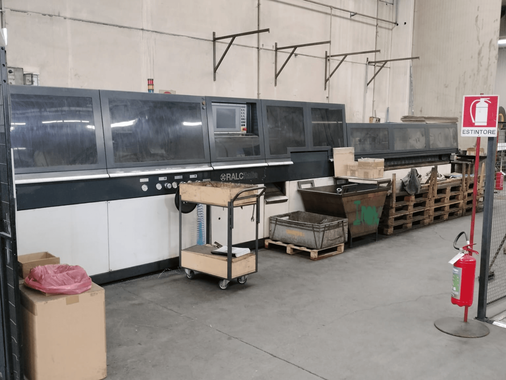 RALC-Industriemaschine in einer Fabrikhalle, Vorderansicht, Bedienfeld sichtbar; Holzpaletten und Feuerlöscher in der Nähe.