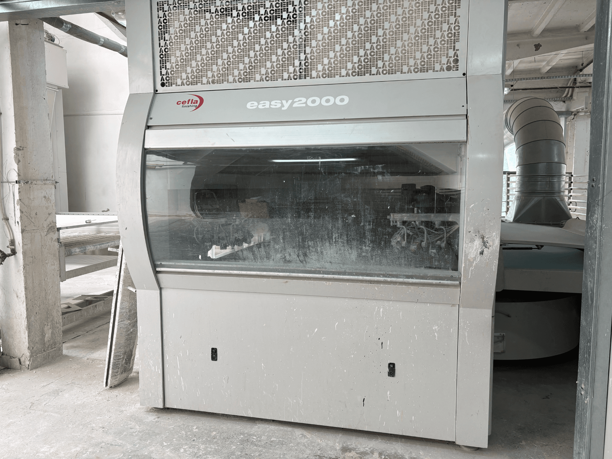 Die Maschine Cefla EASY 2000 D in der Vorderansicht, mit einer großen transparenten Verkleidung, einer staubigen Oberfläche und sichtbaren inneren Bauteilen.