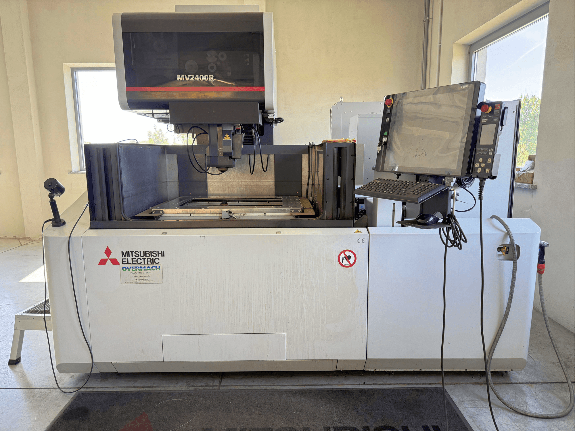Mitsubishi MV2400R-Drahterodiermaschine in Frontansicht, mit Bedienfeld, Arbeitsbereich und Sicherheitsbeschilderung.