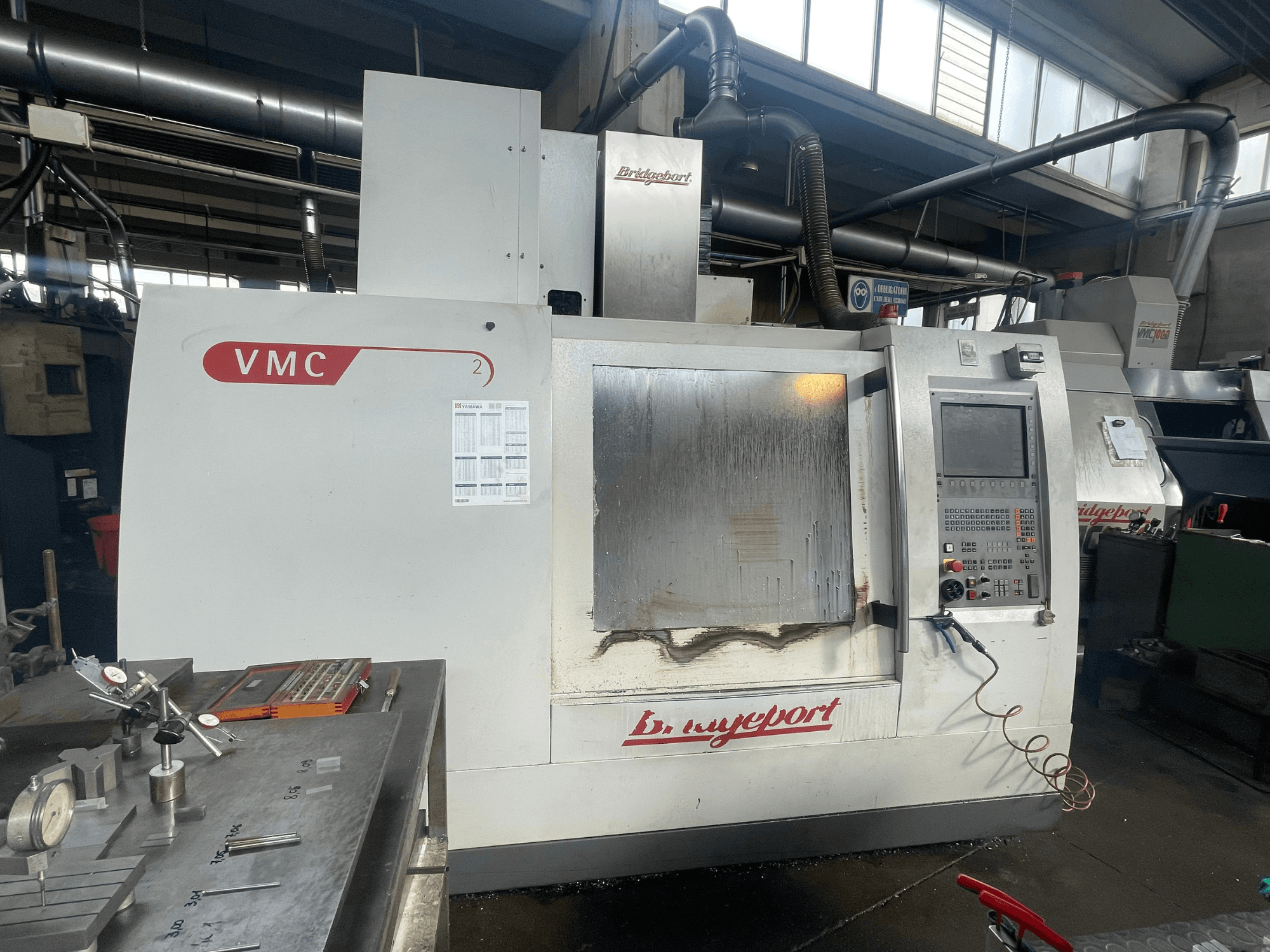 Vertikales Bearbeitungszentrum Bridgeport VCM 800-30 in einer Werkstatt, mit Bedienfeld und Werkzeugtisch. Vorderansicht mit sichtbaren Details.