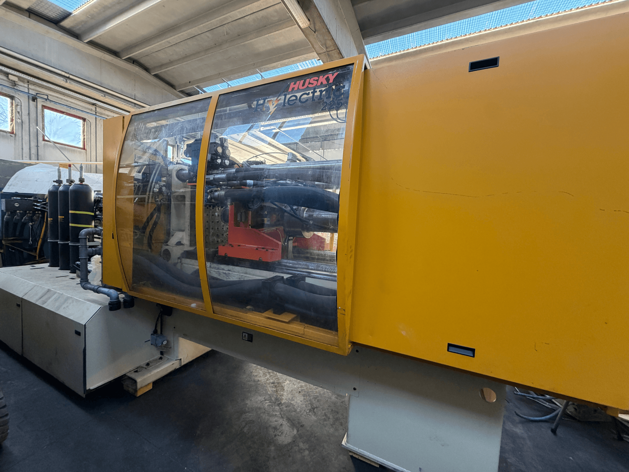 Elektrische Spritzgießmaschine Husky HL225 RS65, Vorderansicht mit gelbem Gehäuse, sichtbarem Bedienfeld und Hydraulikkomponenten.