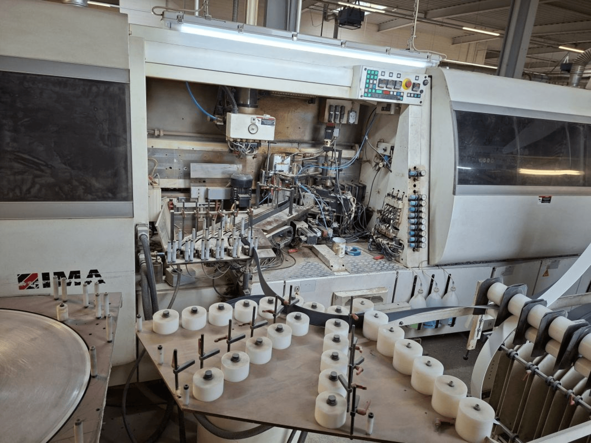 IMA-Maschinen von der Seite betrachtet, mit komplexen mechanischen Komponenten und einem runden Tisch mit weißen Spulen.