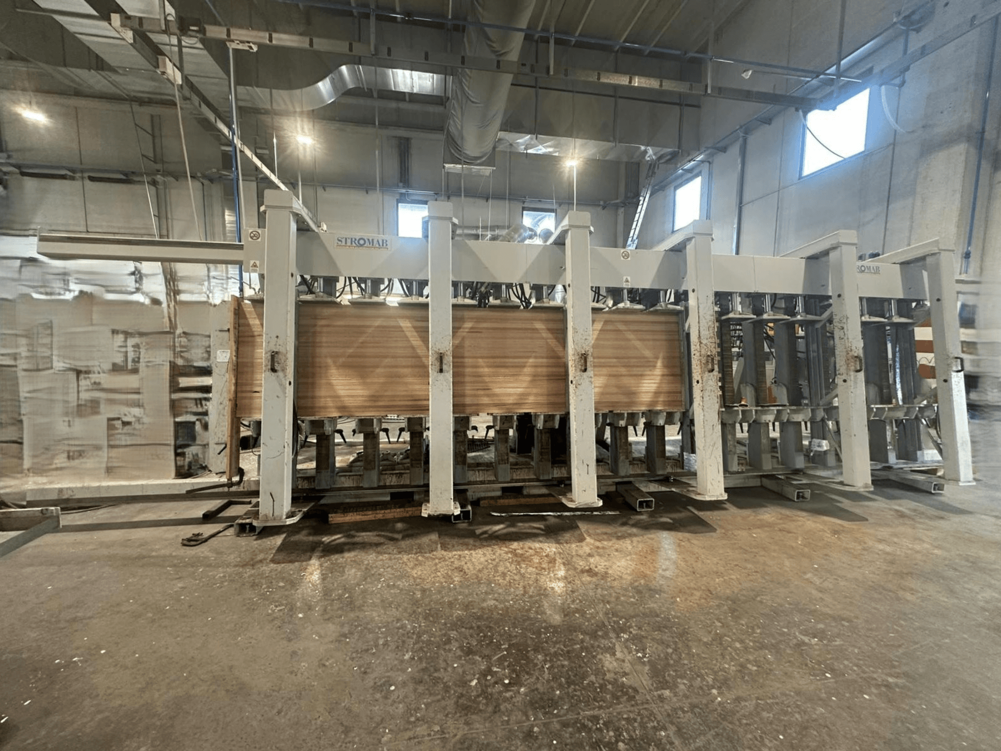 Industrielle STROMAB-Maschine in einer Lagerhalle, Vorderansicht, mit Holzplatten, die bearbeitet werden, Metallstruktur und mechanische Teile.