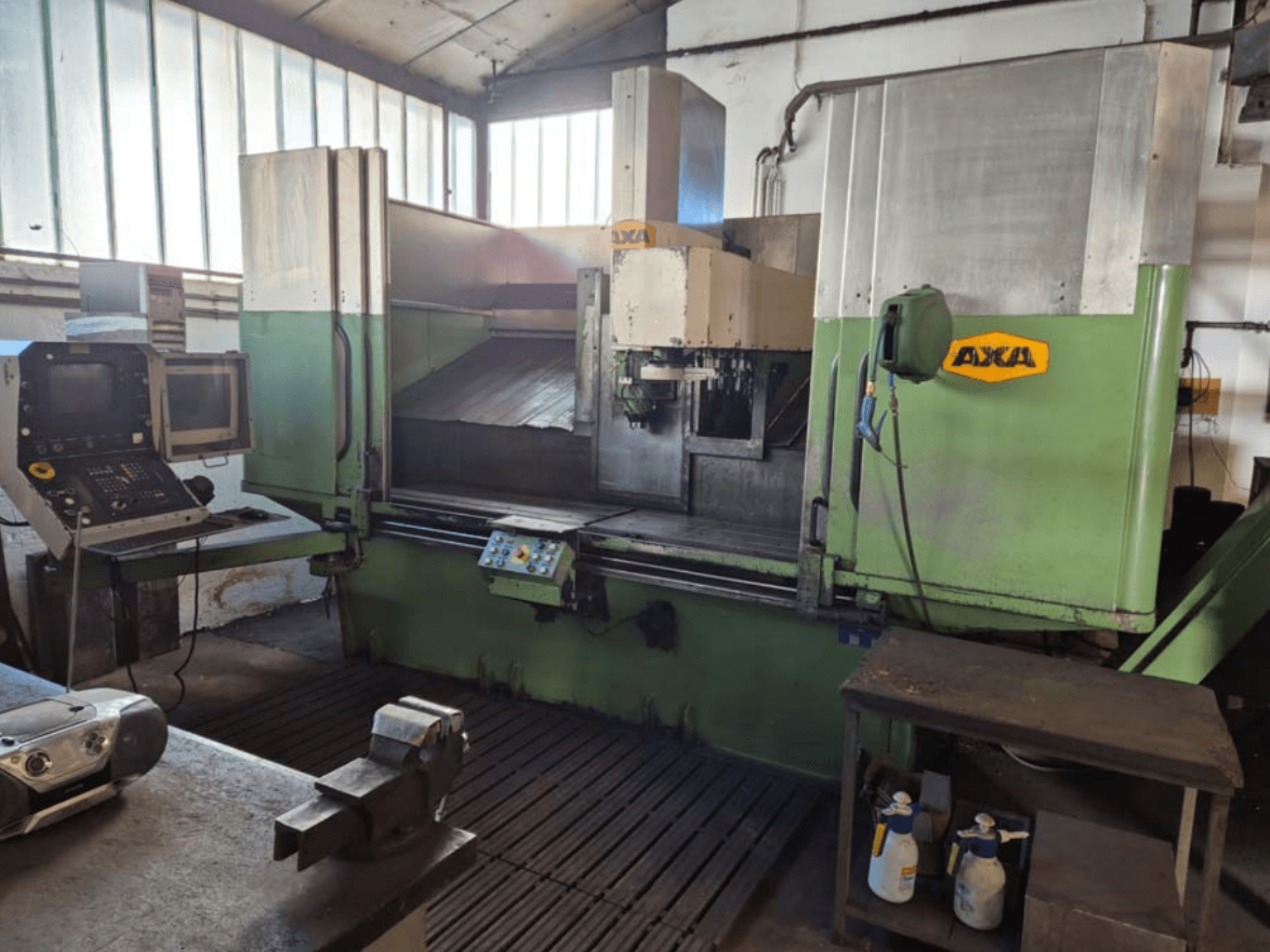 Vertikales Bearbeitungszentrum AXA VSC-2M, Vorderansicht, mit Bedienfeld und Arbeitsbereich mit Schneidwerkzeugen und Reinigungsmitteln.