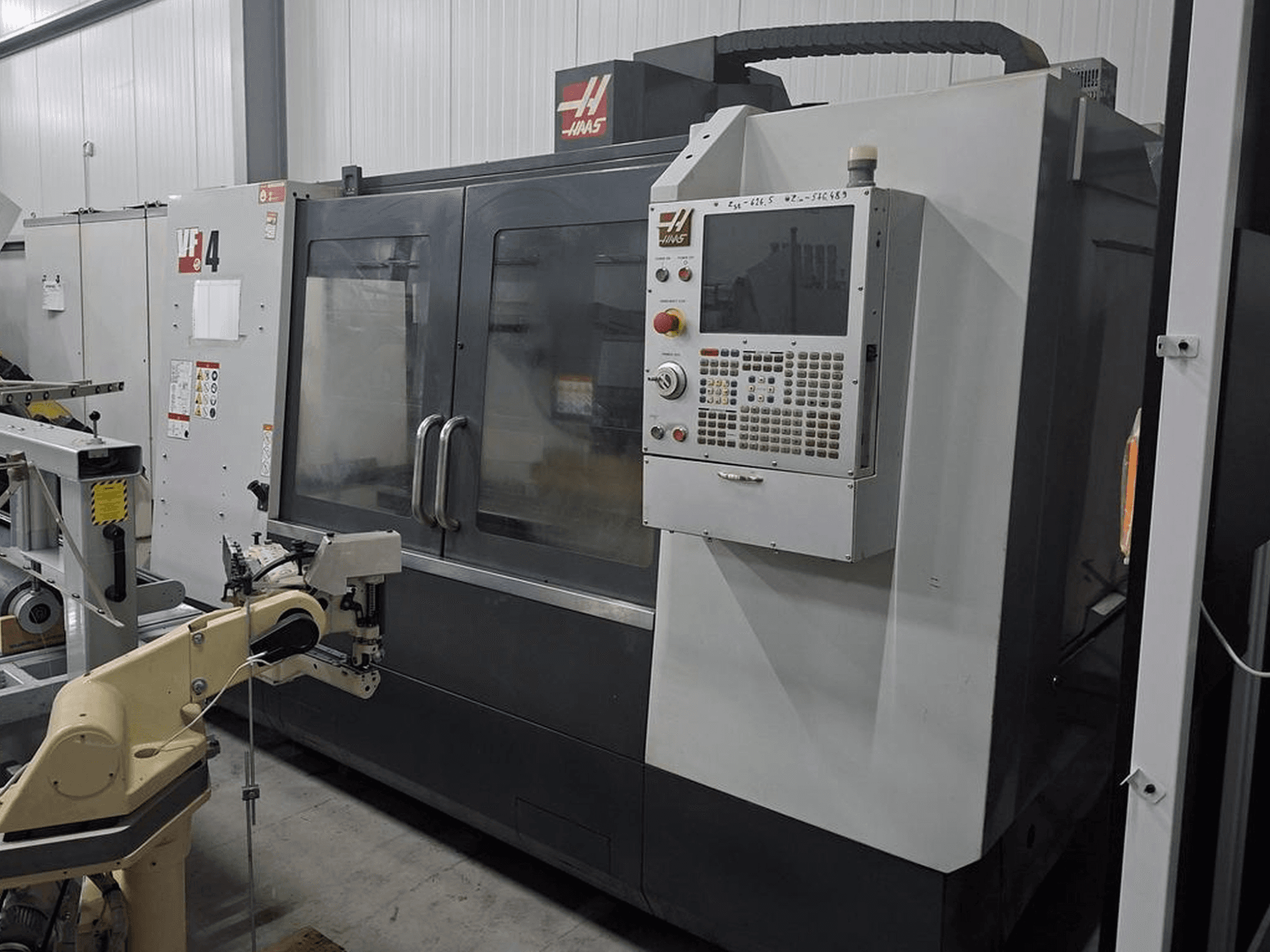 Haas VF-4 CNC-Fräsmaschine in der Vorderansicht, mit numerischer Steuerung und Roboterarm zur Automatisierung.