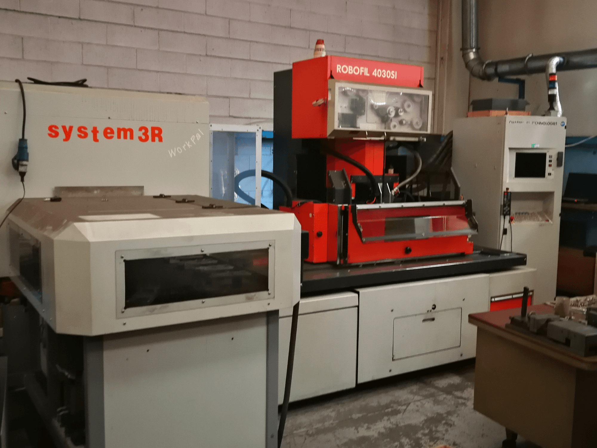 Frontansicht der Drahterodiermaschine CHARMILLES ROBOFIL 4030 Si mit rot-grauem Gehäuse und angrenzendem system3R-Arbeitsplatz.