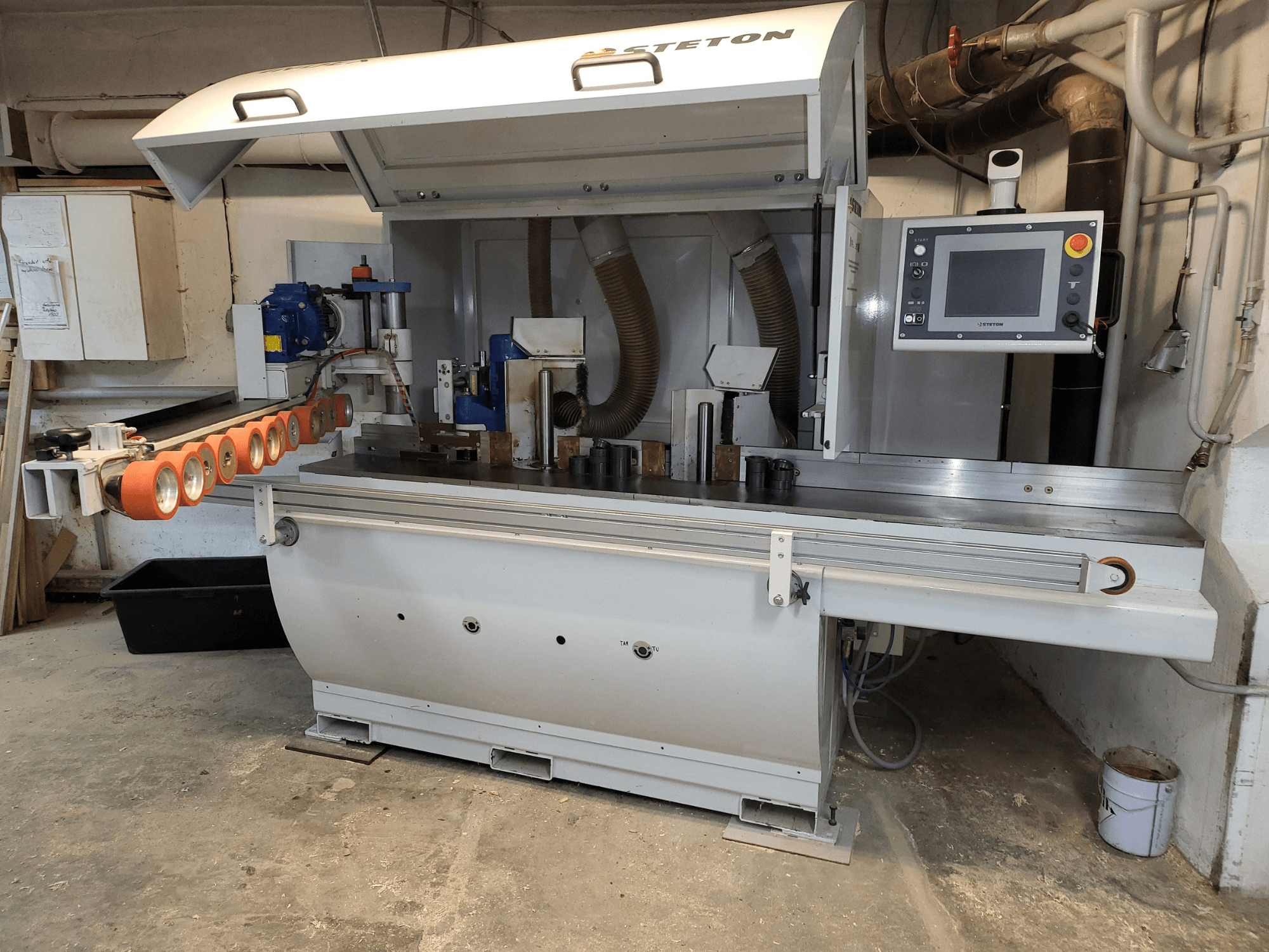 Vorderansicht einer Stetton-Holzbearbeitungsmaschine mit einem Bedienfeld, Zuführungsrohren und verschiedenen Holzstücken auf dem Tisch.