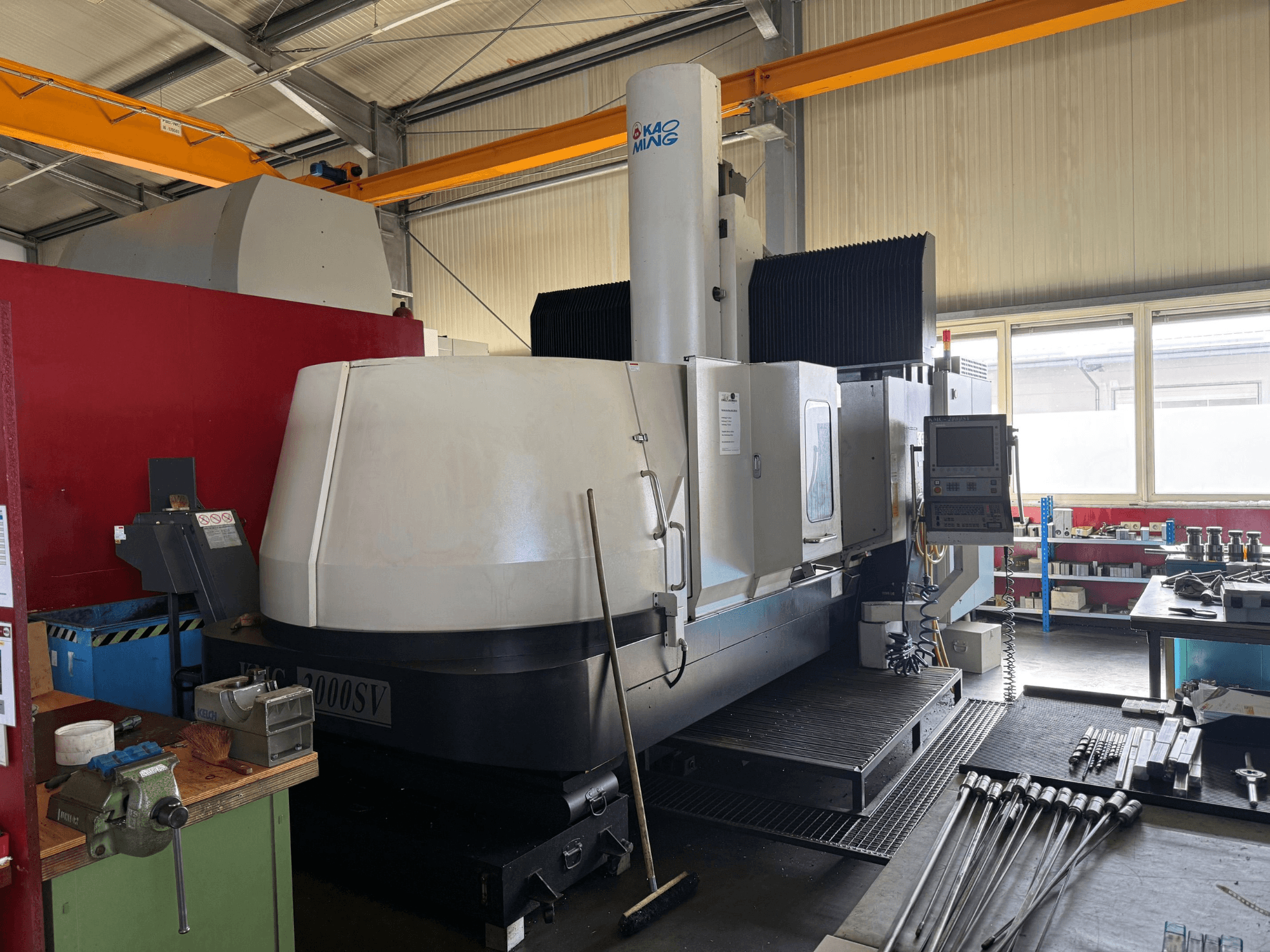 Portalfräsmaschine KAOMING KMC-2000 SV in einer Werkstatt, Vorderansicht mit sichtbarem Bedienfeld und den umliegenden Werkzeugen.