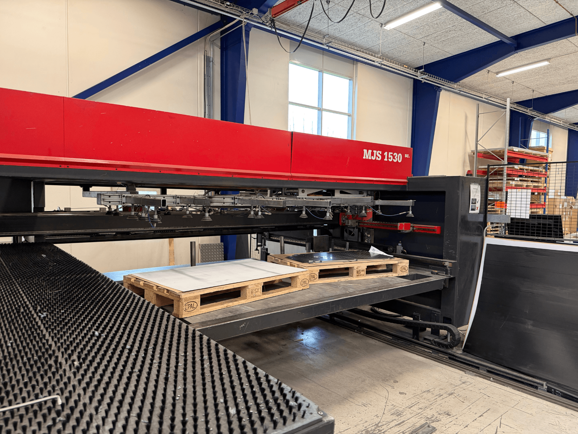 MJS 1530 CNC-Maschine in einer Werkstatt, Vorderansicht, mit einer Holzpalette, die ein Blech auf einer erhöhten Plattform hält.