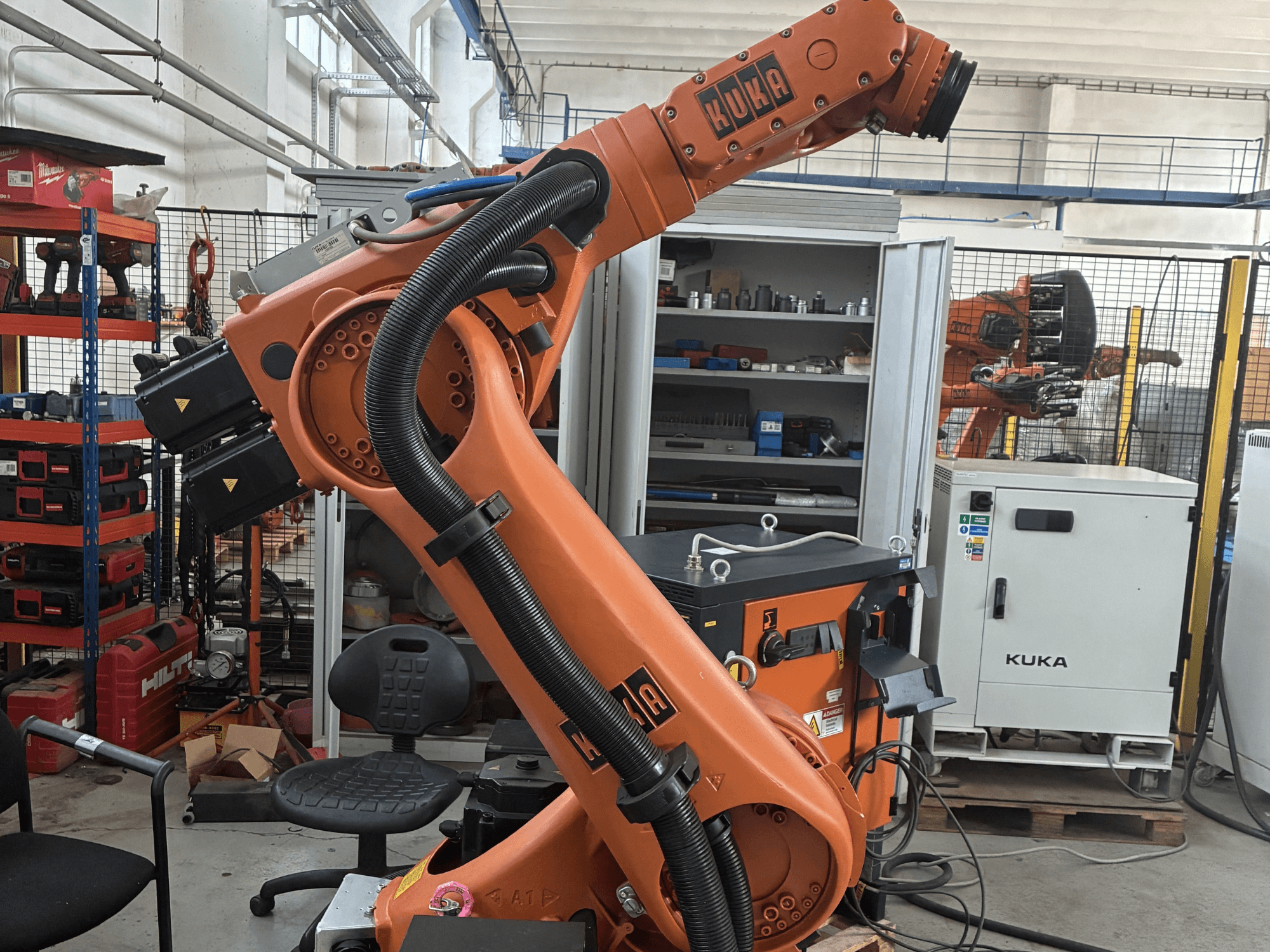 KUKA KR30-3 Roboterarm in einer industriellen Umgebung, Seitenansicht mit Kabeln und Steuerungen, im Hintergrund Werkzeuge und Regale.