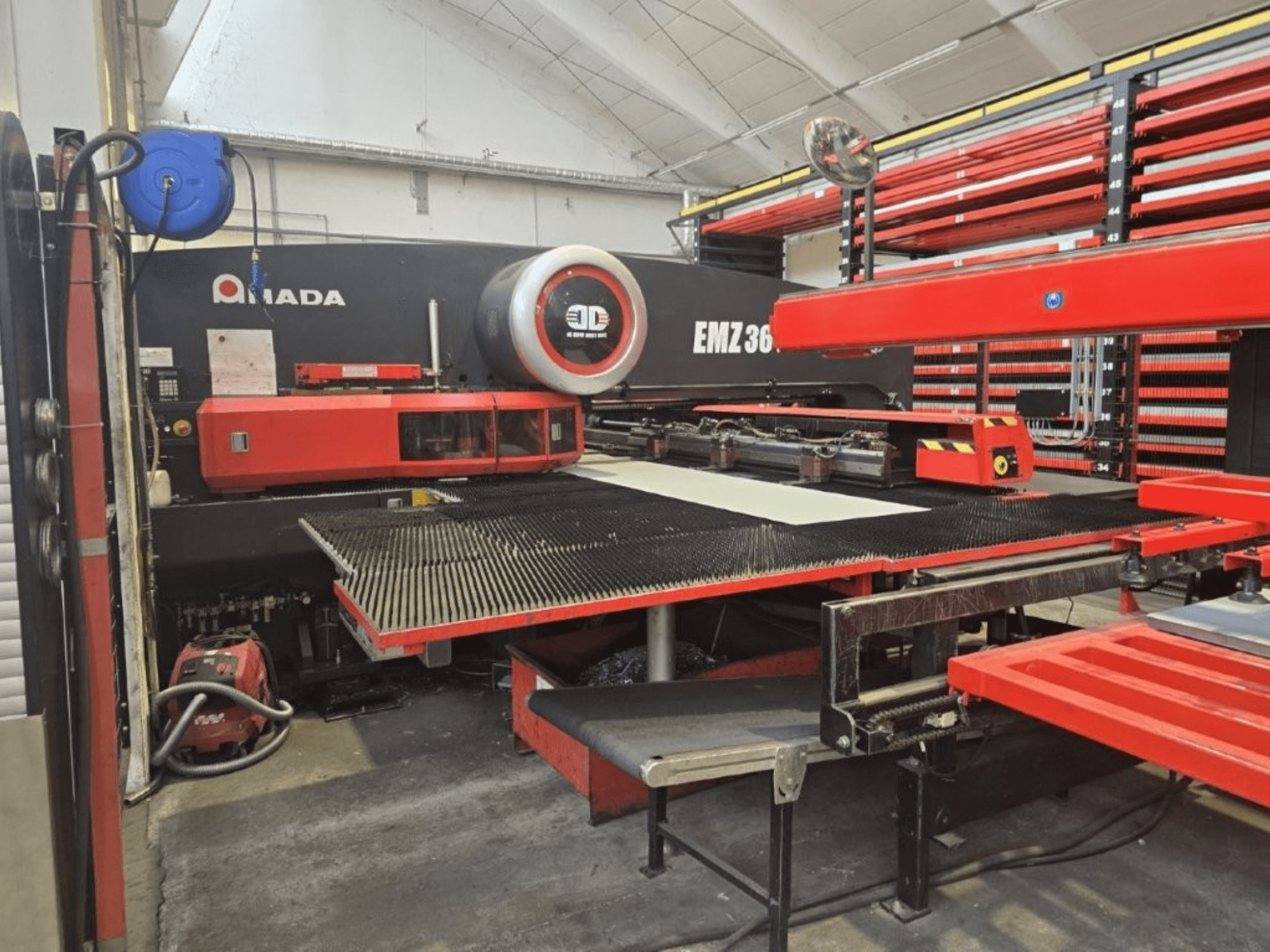 Amada EMZ 36 Laserschneidmaschine in einer Werkstatt, Vorderansicht, mit roten Akzenten und einem großen Schneidtisch.
