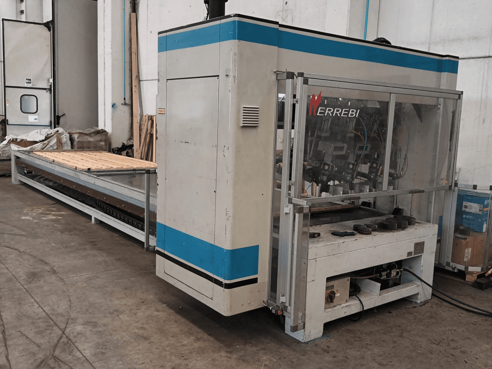 ERREBI-Maschine, Seitenansicht, mit einem großen Bearbeitungstisch mit mechanischen Komponenten und transparenter Schutzabdeckung.