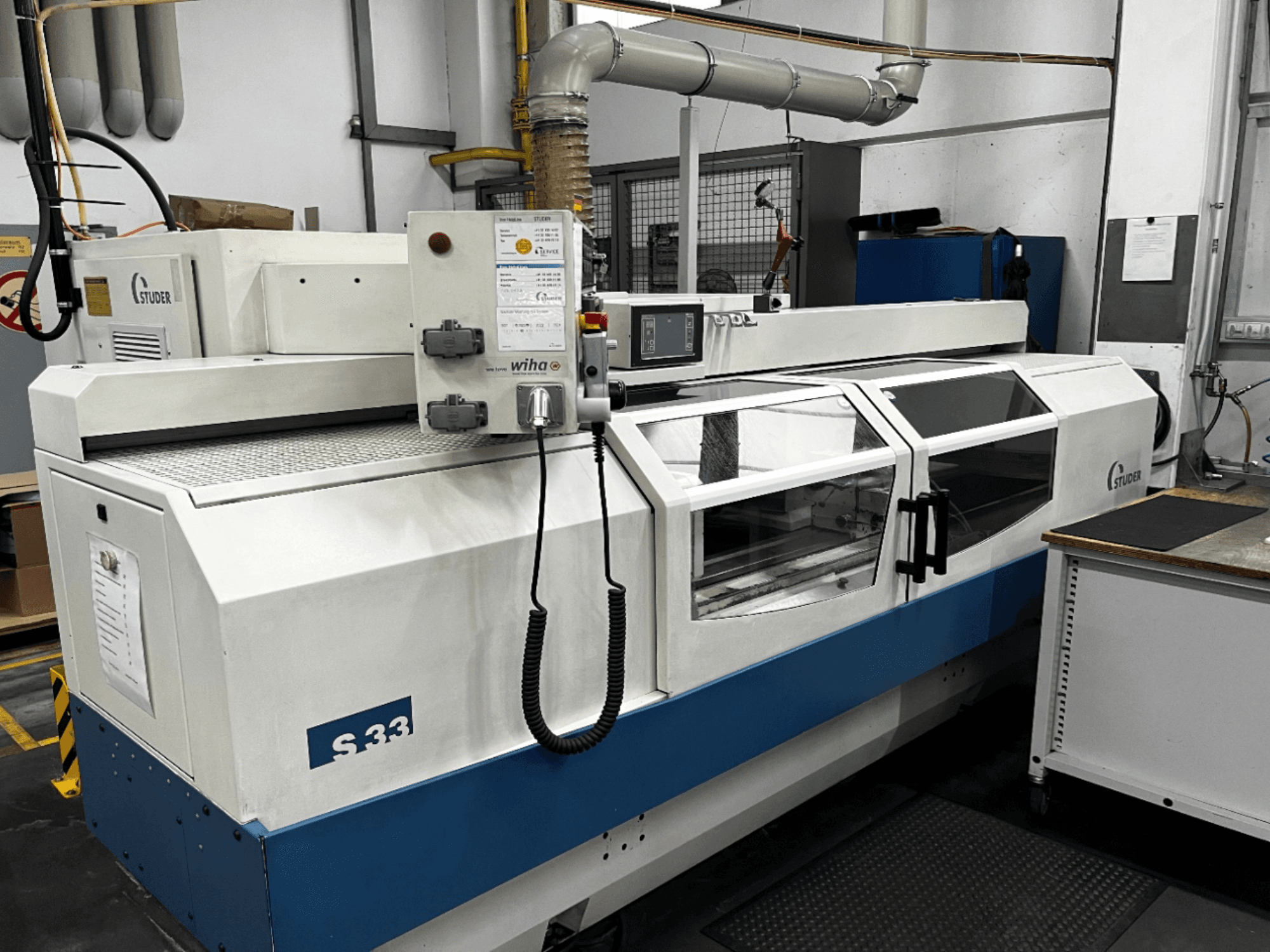 STUDER S33 CNC-Rundschleifmaschine, Vorderansicht; mit Bedienfeld und Schutzglastüren. Industrielle Umgebung.