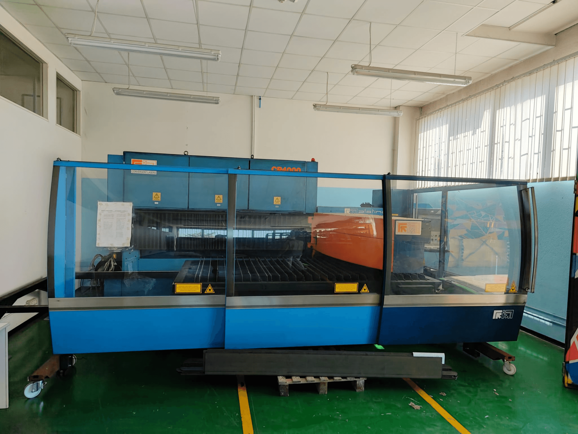 Vorderansicht einer CO₂-Laserschneidmaschine vom Typ CP4000 von CONVERGENT LASERS mit blau-orangefarbenem Design in einer gut beleuchteten Werkstattumgebung.