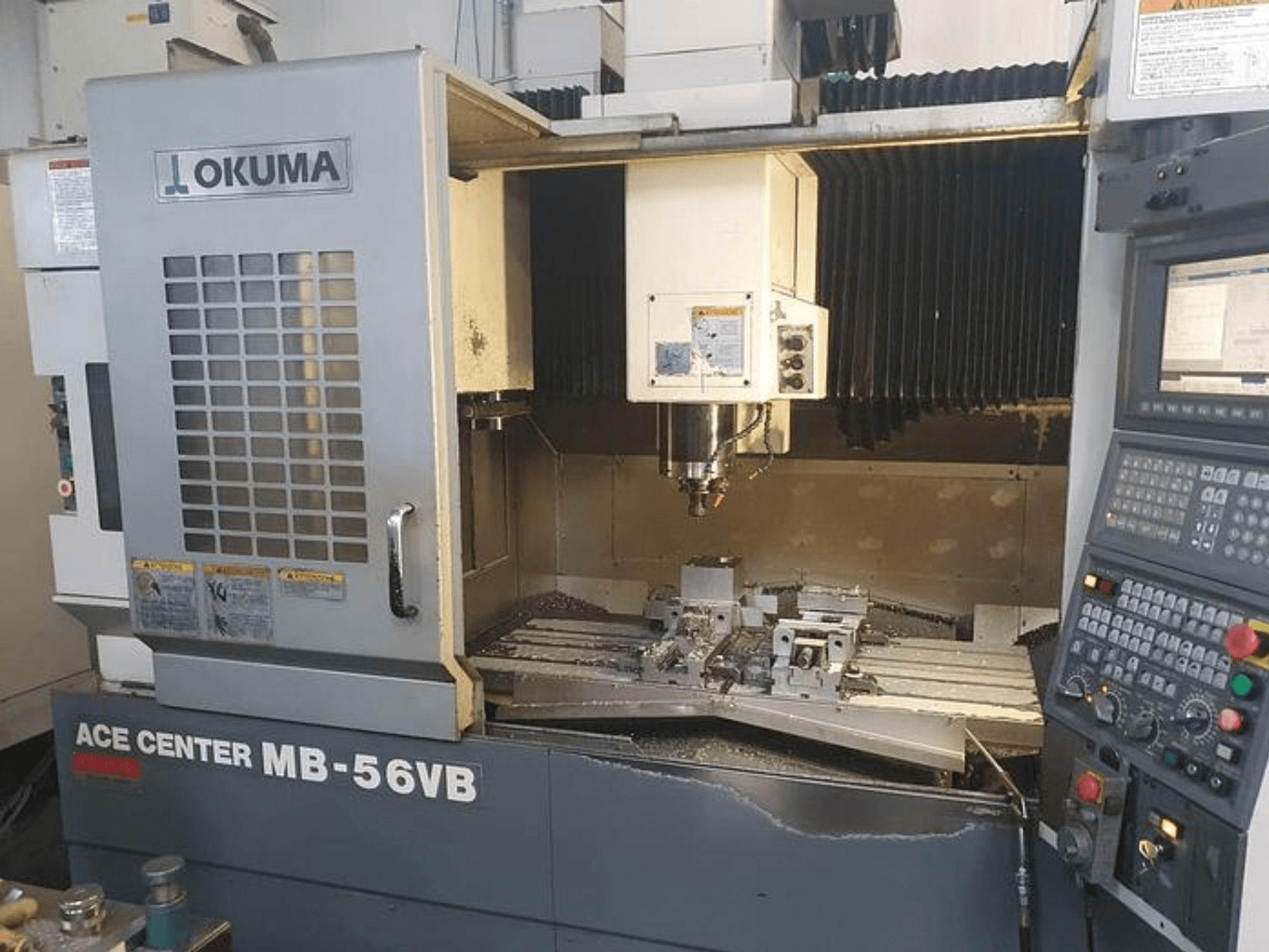 Okuma ACE CENTER MB-56VB CNC-Fräsmaschine in der Frontansicht, die das Bedienfeld und den Bearbeitungsbereich zeigt.