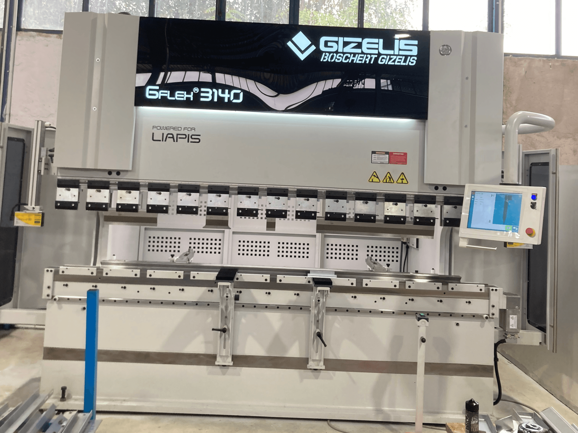 Hydraulische Presse GIZELIS G-FLEX 3140 in Frontansicht mit Kontrollbildschirm, mit mehreren Biegewerkzeugen und Sicherheitsetiketten.