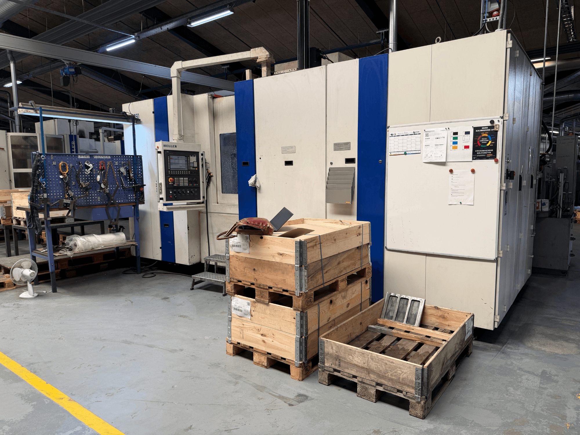 HORIZONTAL-BEARBEITUNGSZENTRUM HELLER MCH 250 in der Werkstatt, Seitenansicht mit Holzpaletten und Werkzeugregal sichtbar.