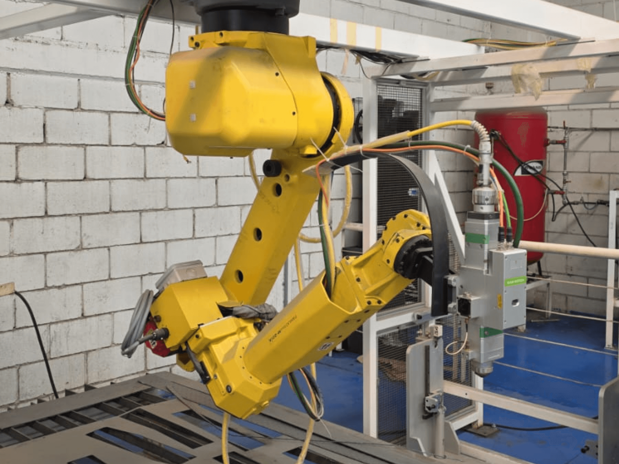 Gelber Roboterarm mit einem Präzisionswerkzeug, mit mehreren Gelenken und Kabeln, von vorne gesehen in einer Industrieumgebung.