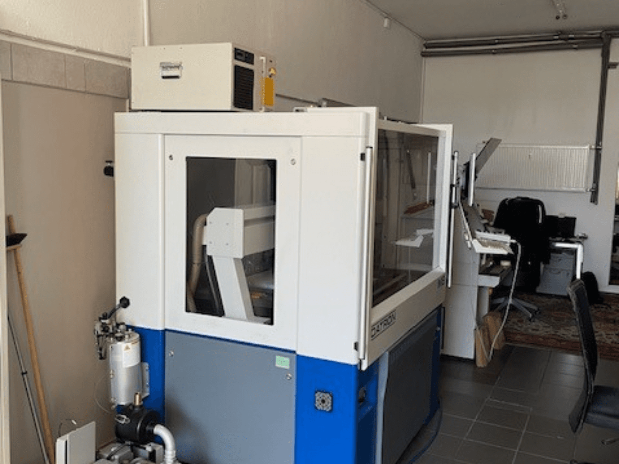 Blau-weiße Industriemaschine mit transparenten Paneelen, Frontansicht, mit Zugang zur Steuerung und sichtbarer Lüftungseinheit.