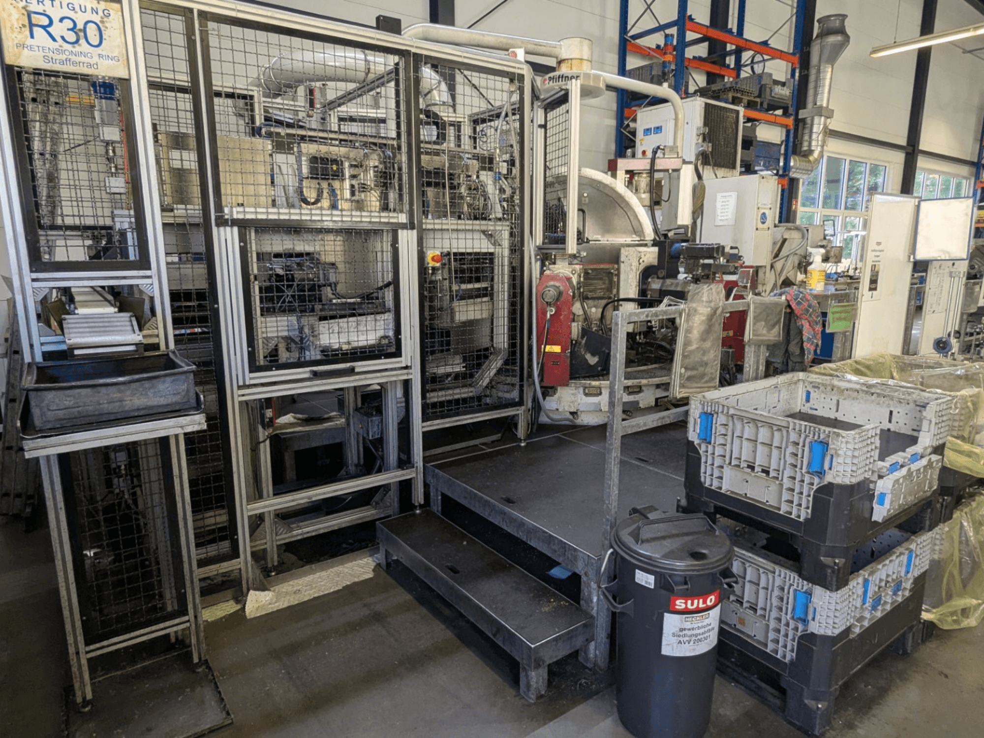 PFIFFNER HB 32/16-Werkzeugmaschine in einer Werkstatt, Vorderansicht mit Blick auf den Produktionsbereich mit Behältern und Sicherheitszaun.