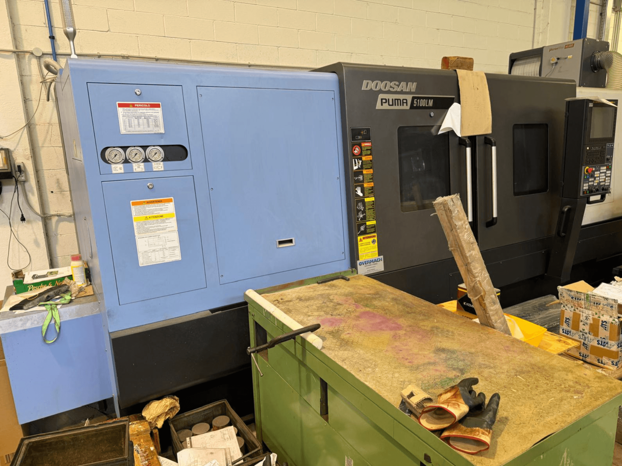 Doosan Puma 5100LM CNC-Maschine und Bedienfeld, Seitenansicht. Auf der blauen Steuereinheit sind Messgeräte und Warnhinweise sichtbar.