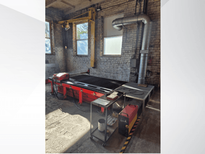 Roter CNC-Plasmaschneidetisch mit Bedienfeld und Metallabsaugung, von der Seite gesehen in einer gut beleuchteten Werkstatt.